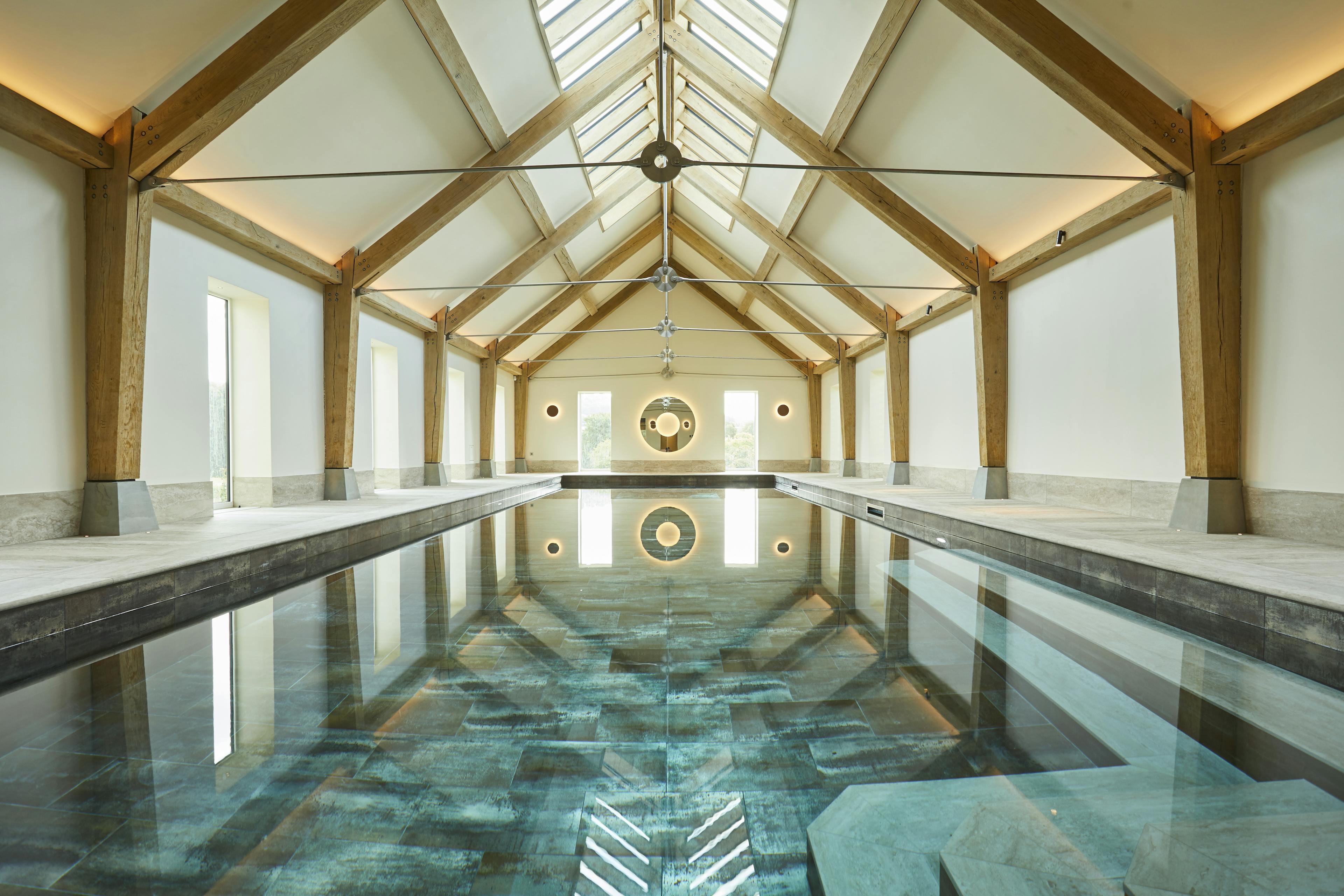 A swimming pool with an oak frame and steel tie connections, windows on the side and rooflights