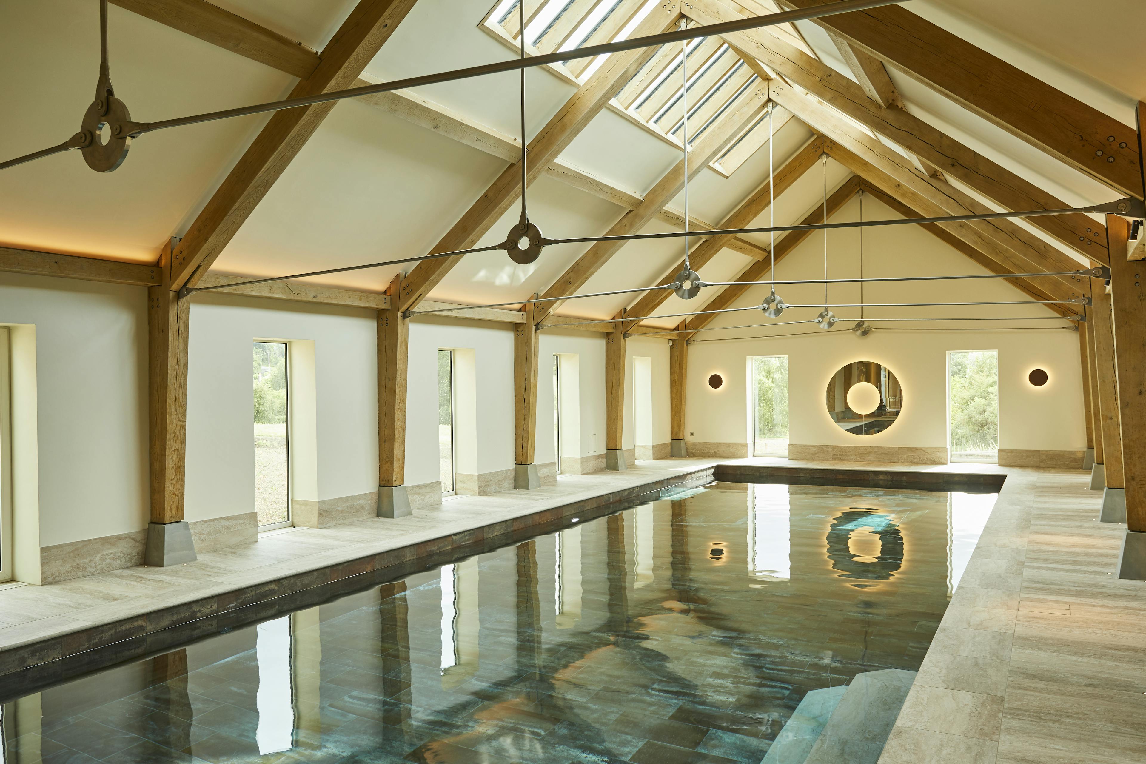 A swimming pool with an oak frame and steel tie connections, windows on the side and rooflights