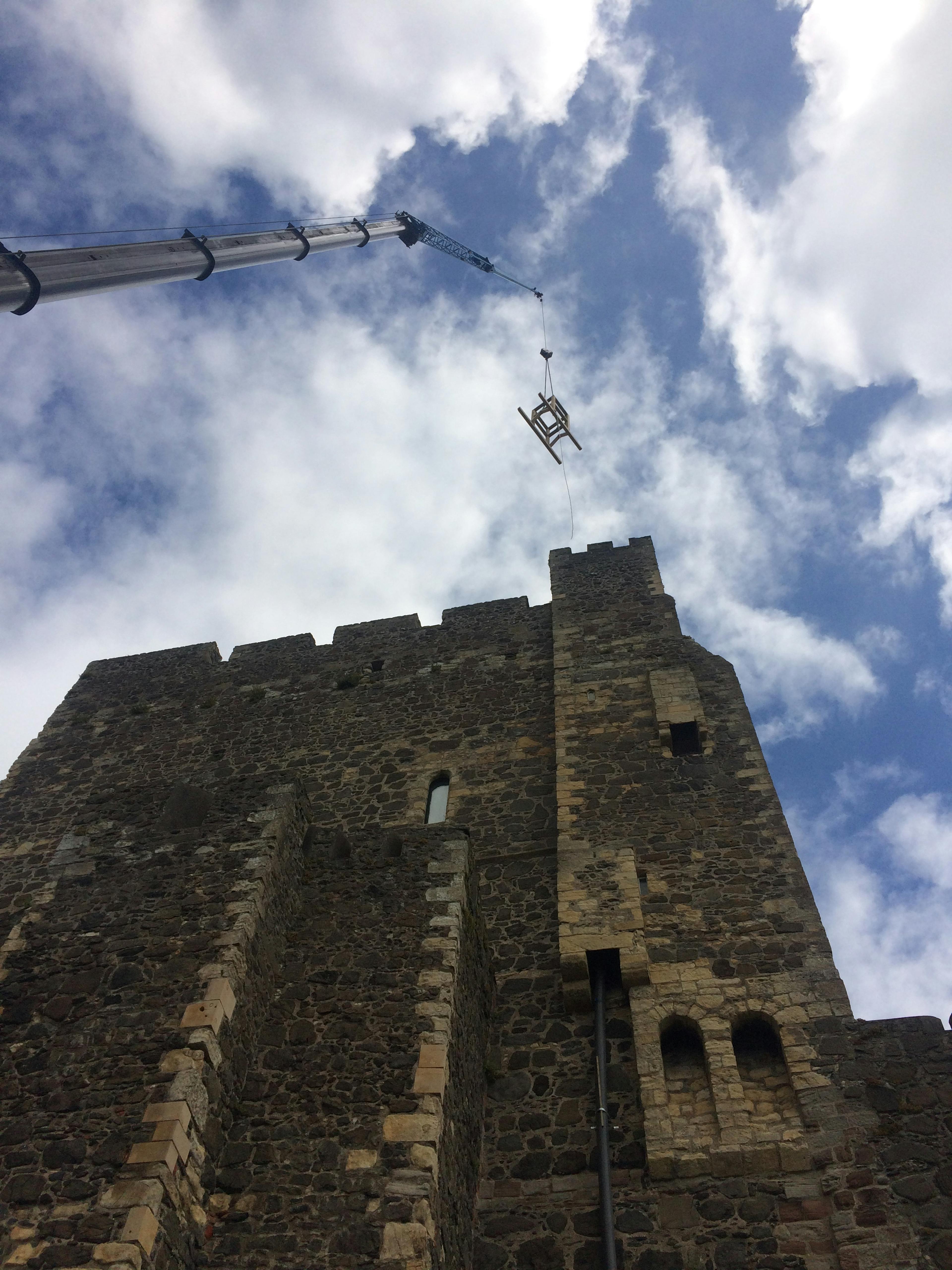 A piece of oak frame is lifted up by a crane onto a stone tower of a 12th century castle