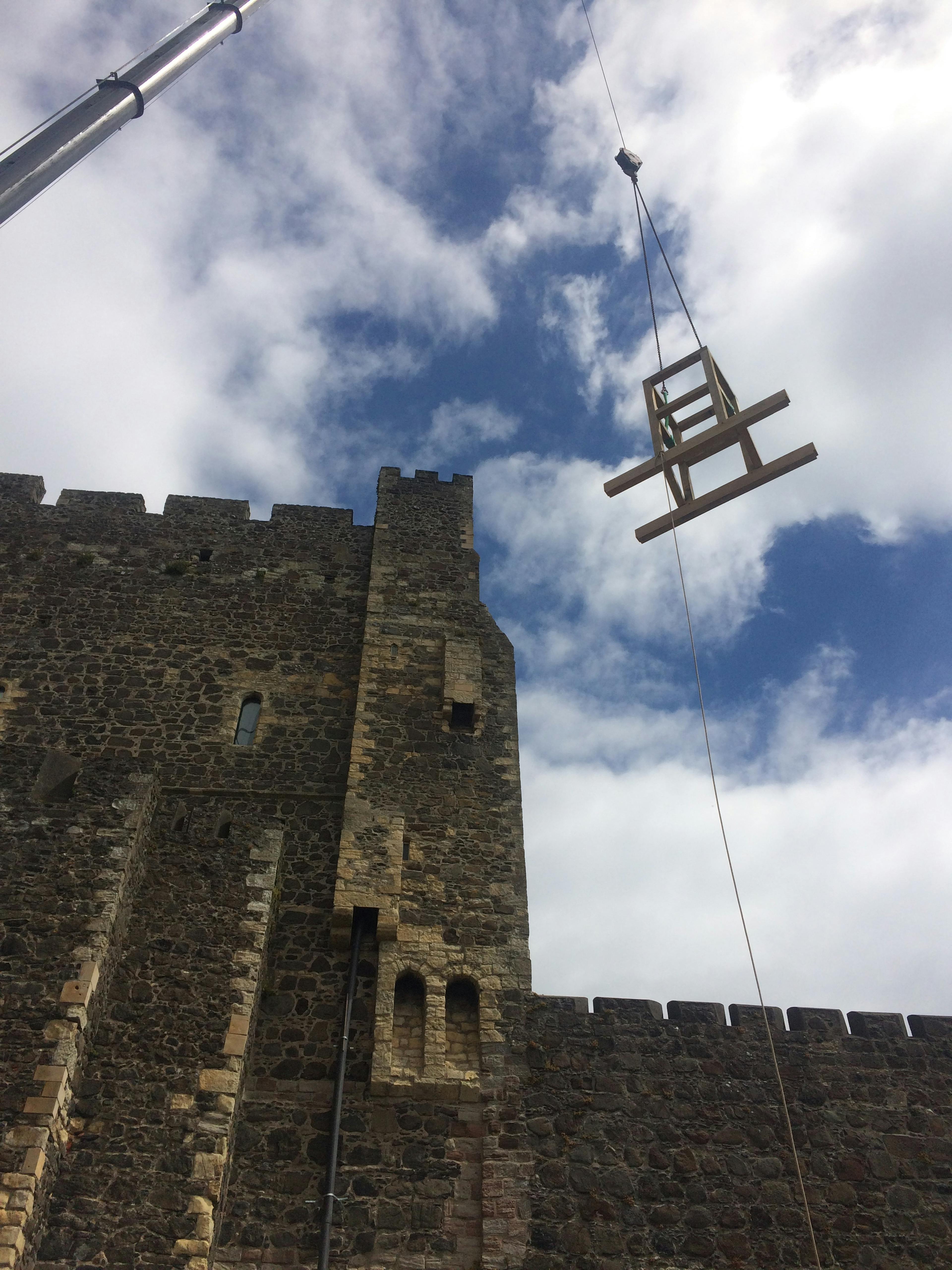 A piece of oak frame is lifted up by a crane onto a stone tower of a 12th century castle