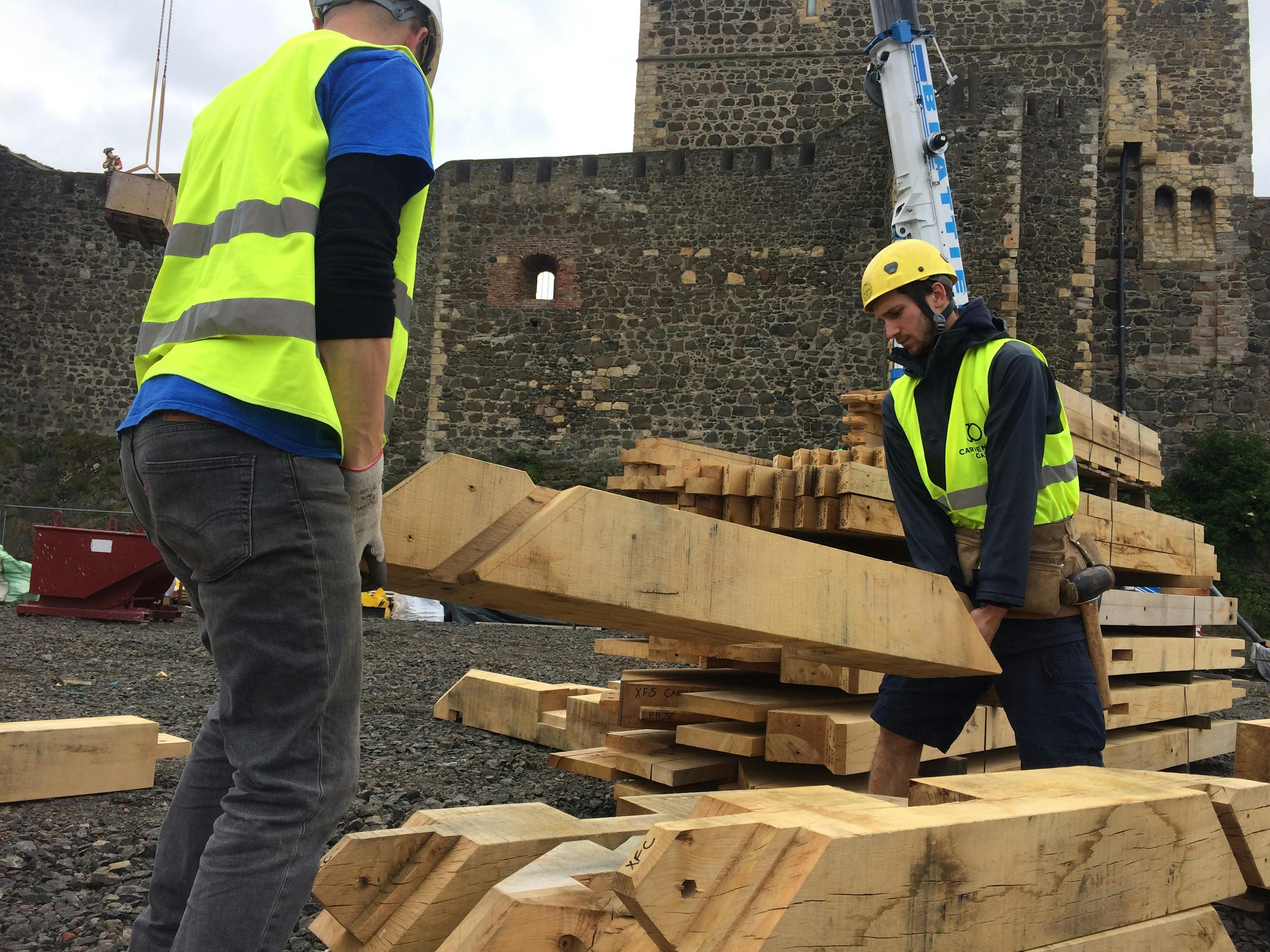 Two carpenters on site move large oak posts for the great hall roof at Carrickfergus Castle in Northern Ireland