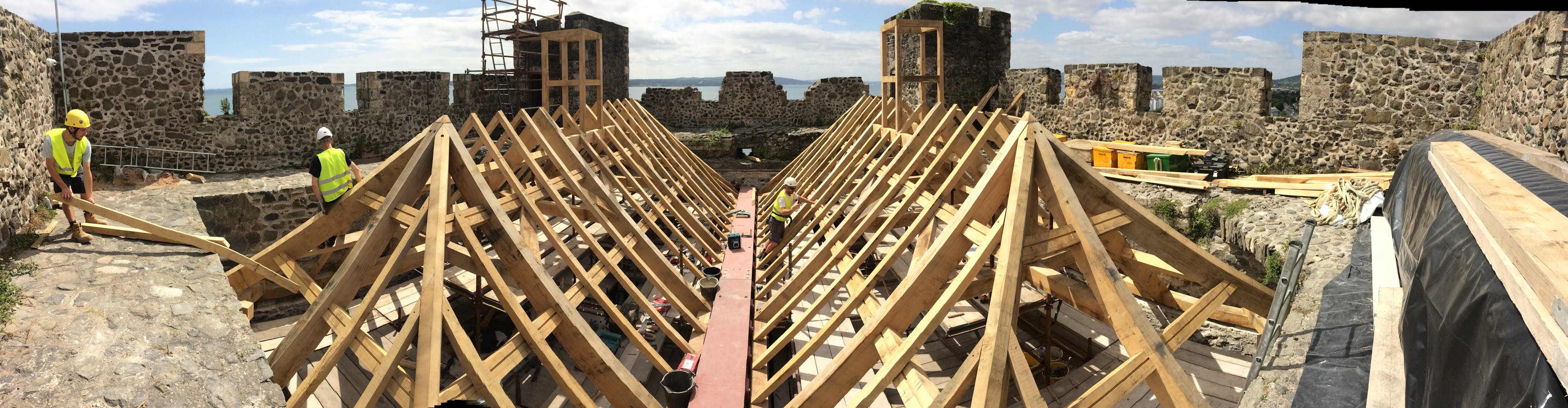 Carpenters work on installing an oak frame at the top of a stone tower of a castle