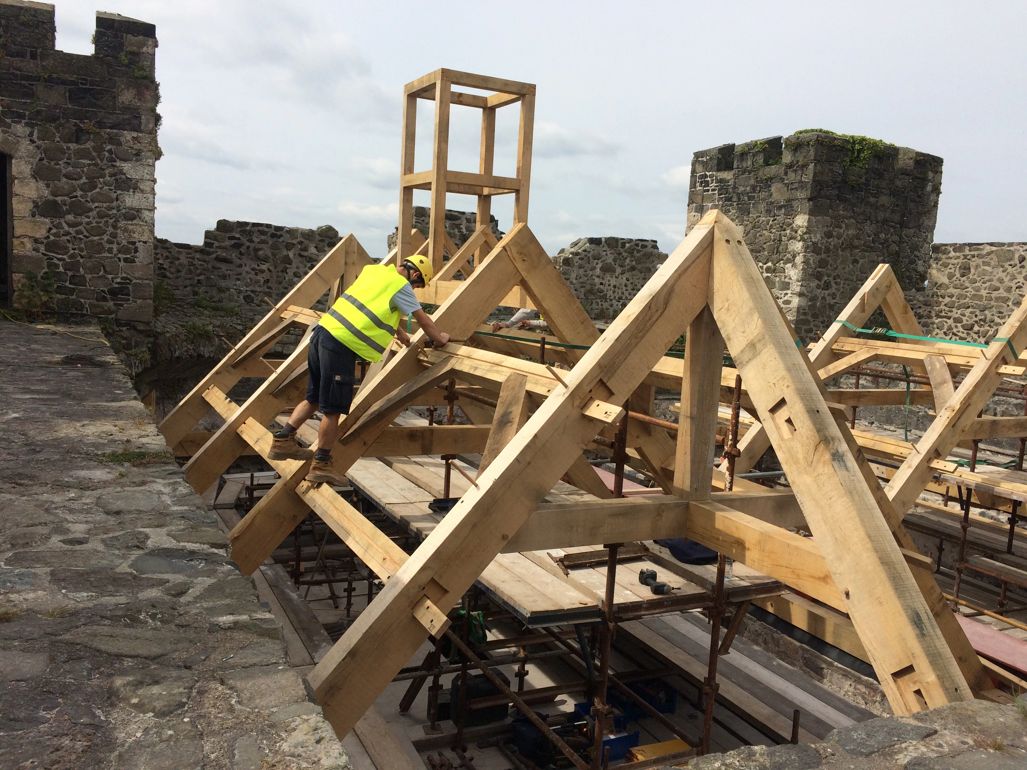 Carpenters work on installing an oak frame at the top of a stone tower of a castle
