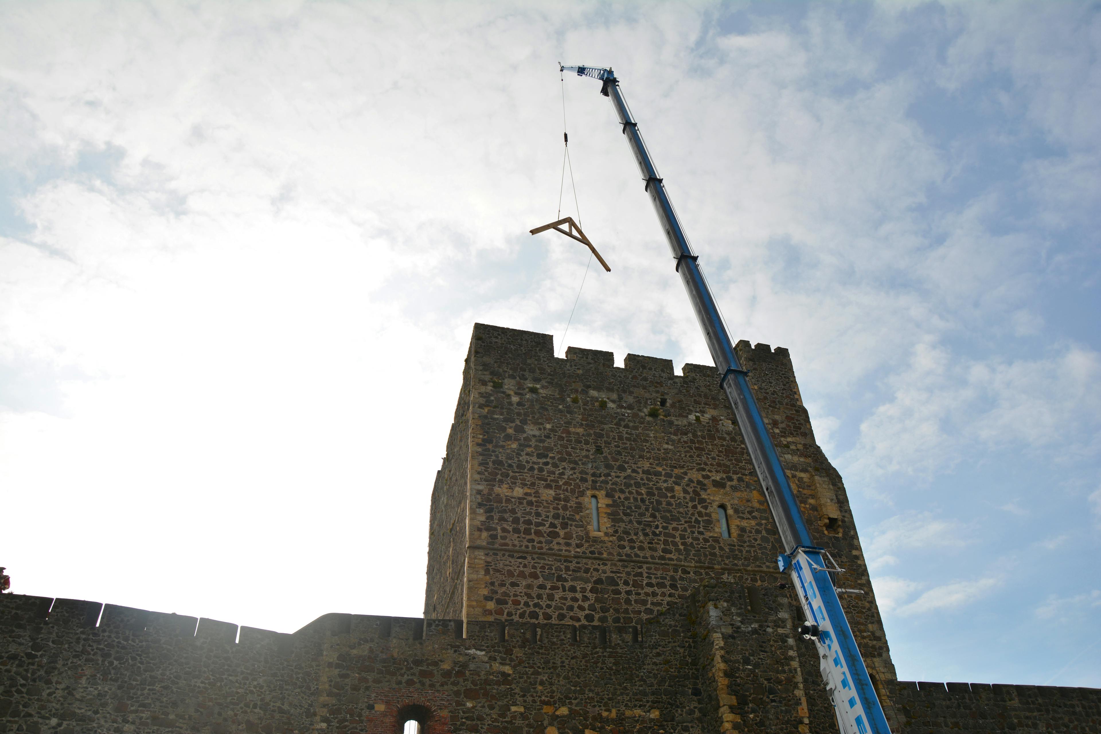 A piece of oak frame is lifted up by a crane onto a stone tower of a 12th century castle