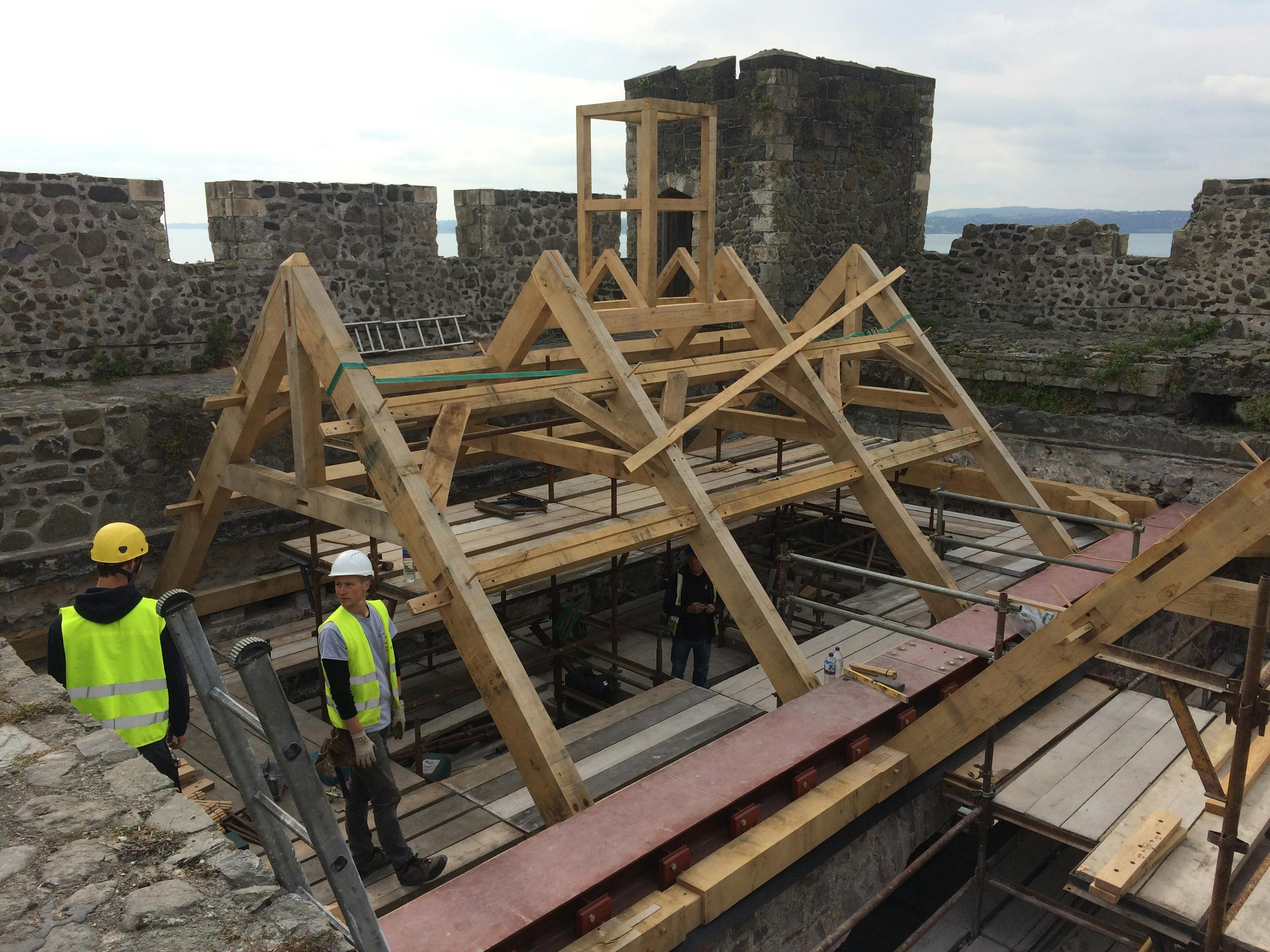 Carpenters work on installing an oak frame at the top of a stone tower of a castle