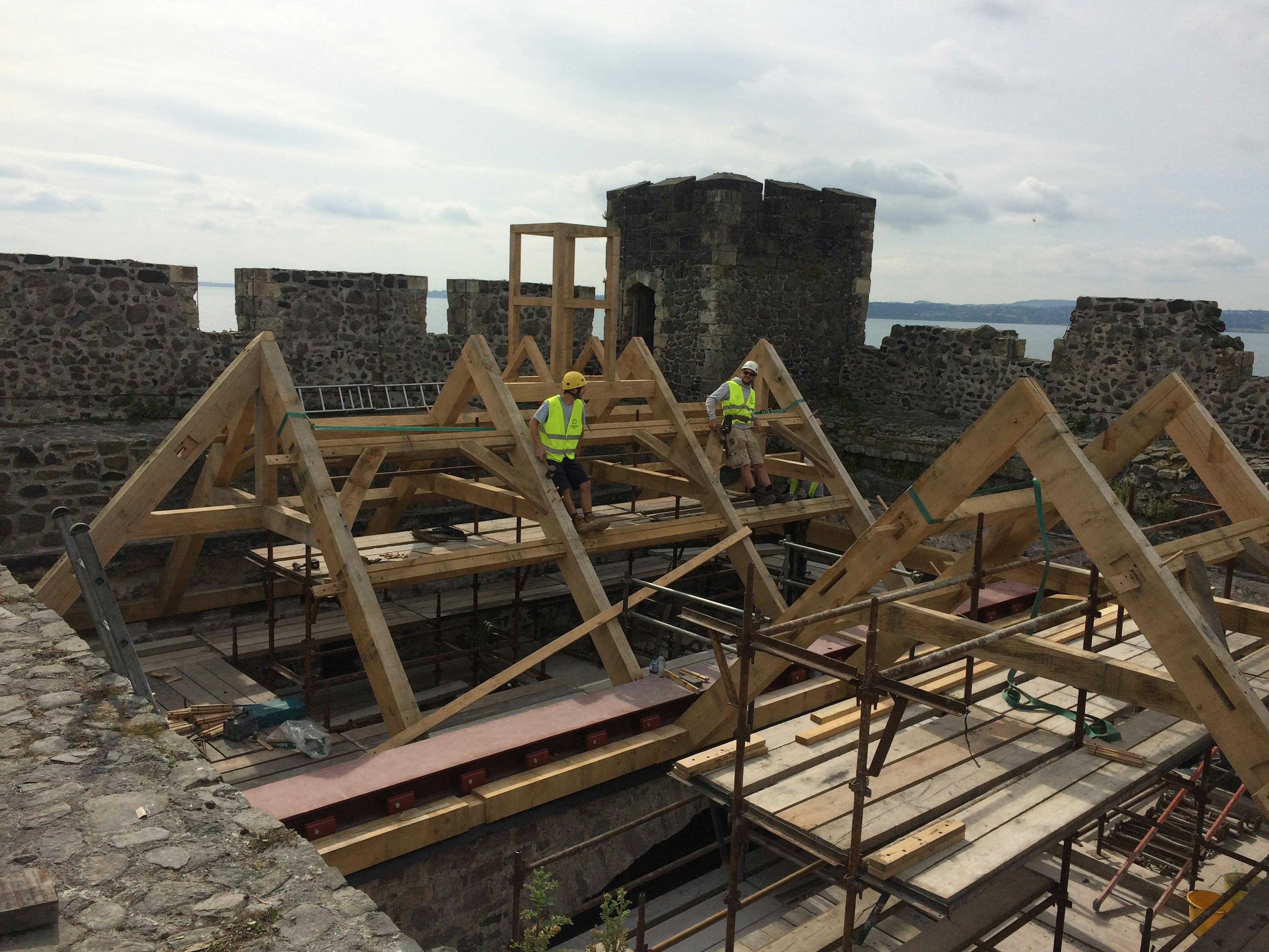 Carpenters work on installing an oak frame at the top of a stone tower of a castle