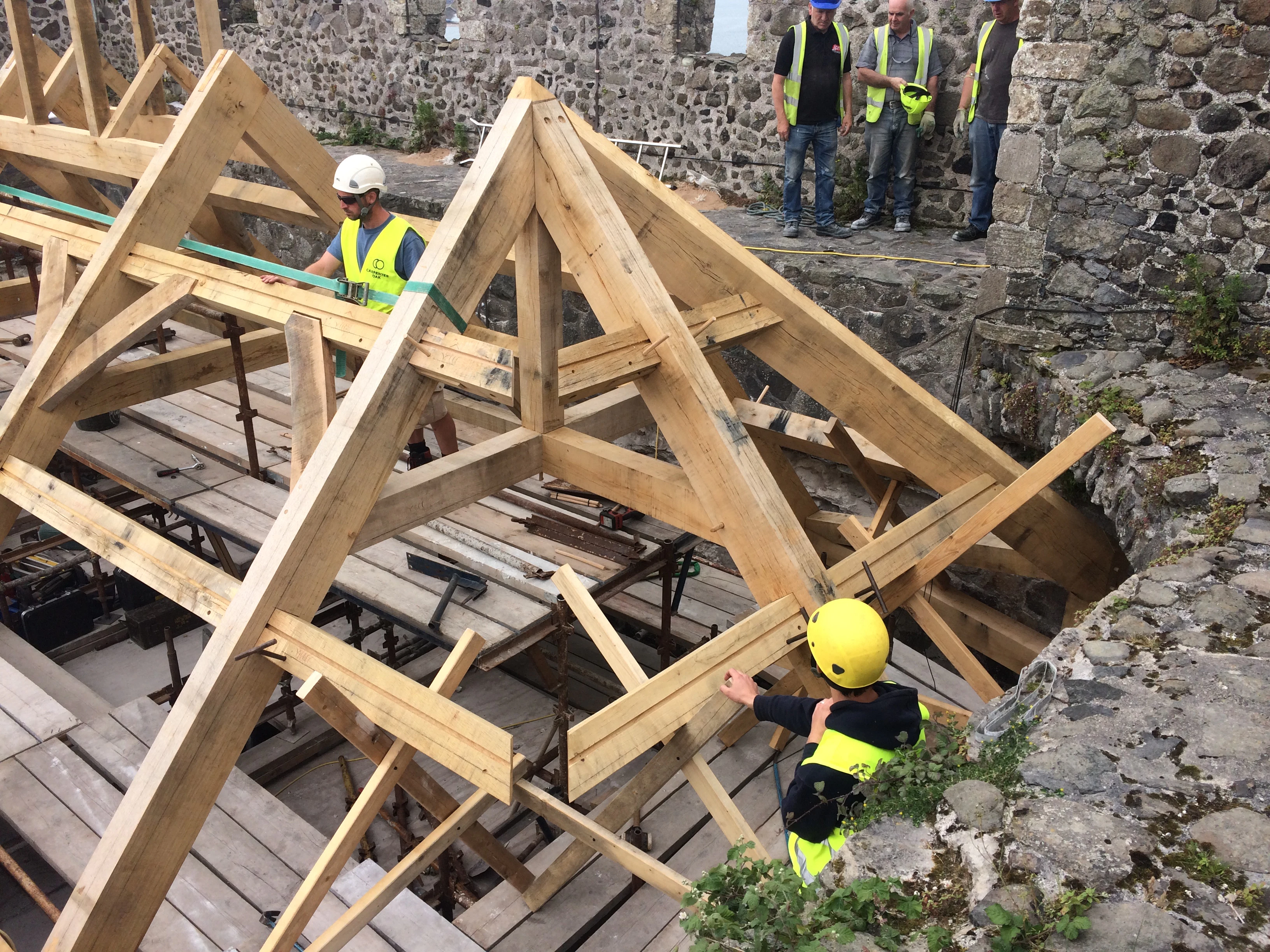 Carpenters work on installing an oak frame at the top of a stone tower of a castle