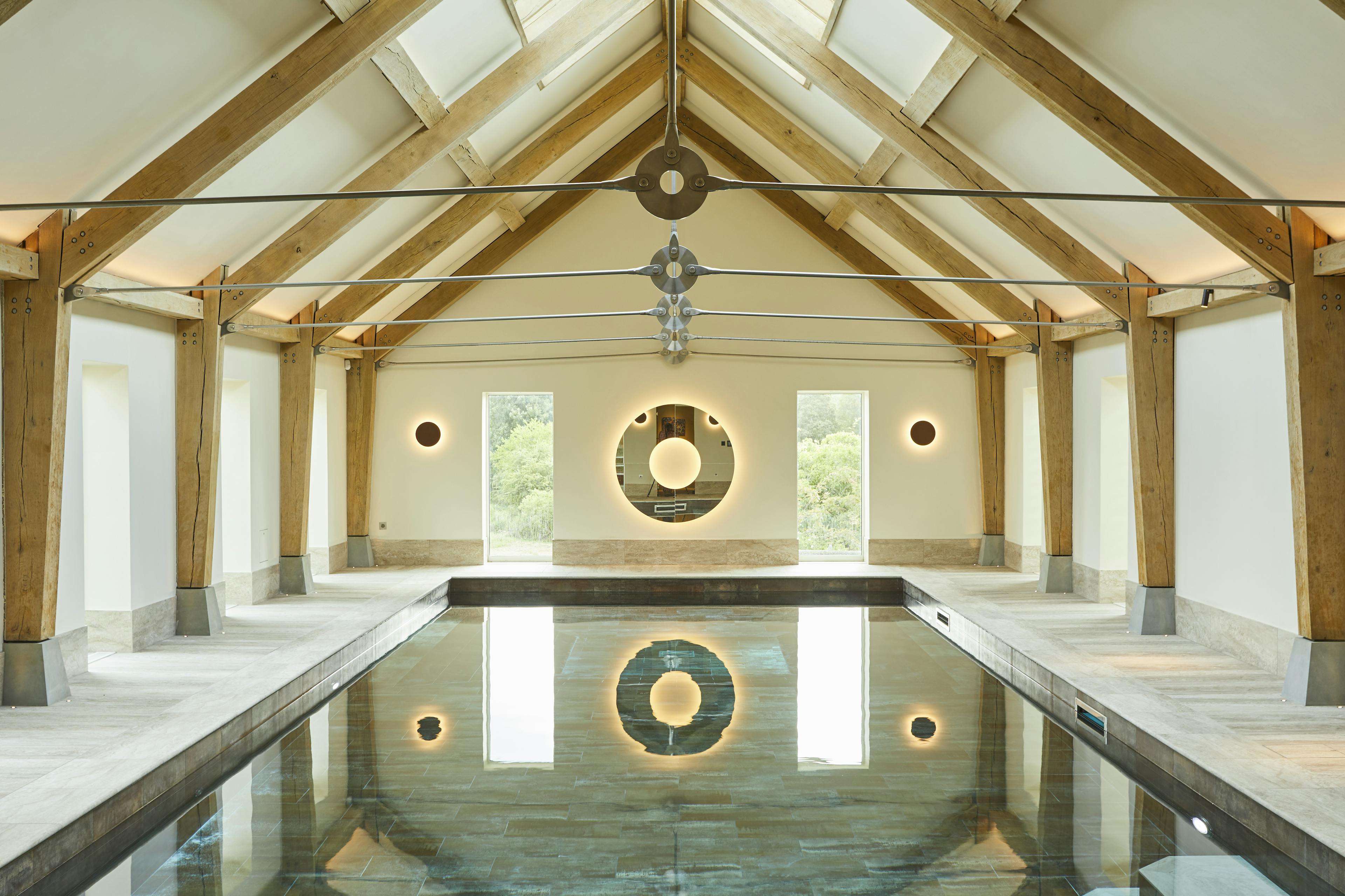 A swimming pool with an oak frame and steel tie connections, windows on the side and rooflights