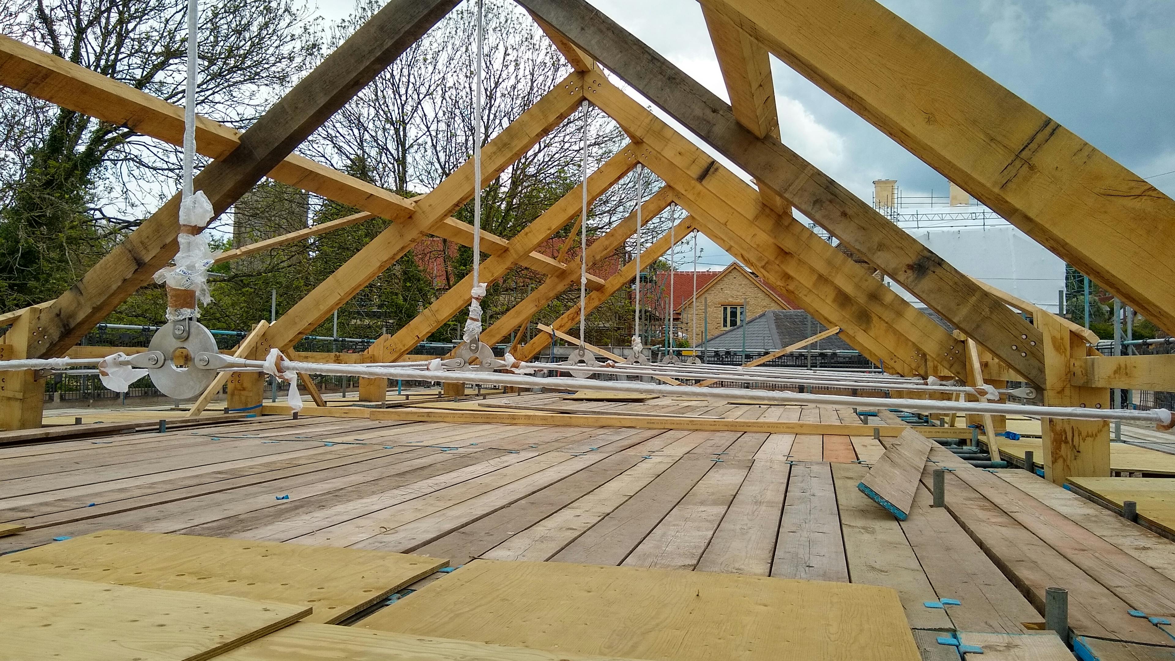 An oak frame roof with steel tie connections being installed on a construction site