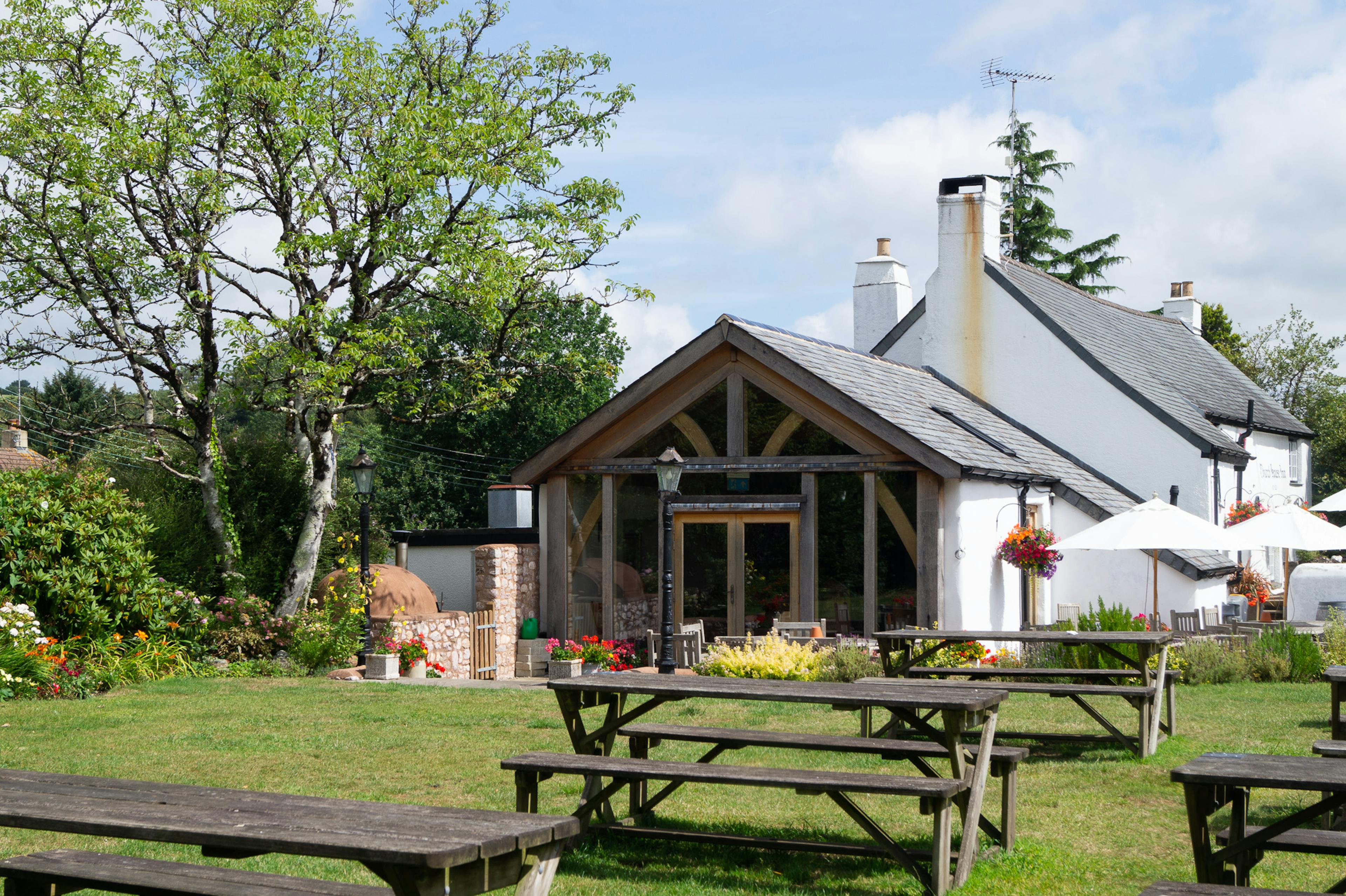 A pub garden with a green lawn and tables with an oak framed extension