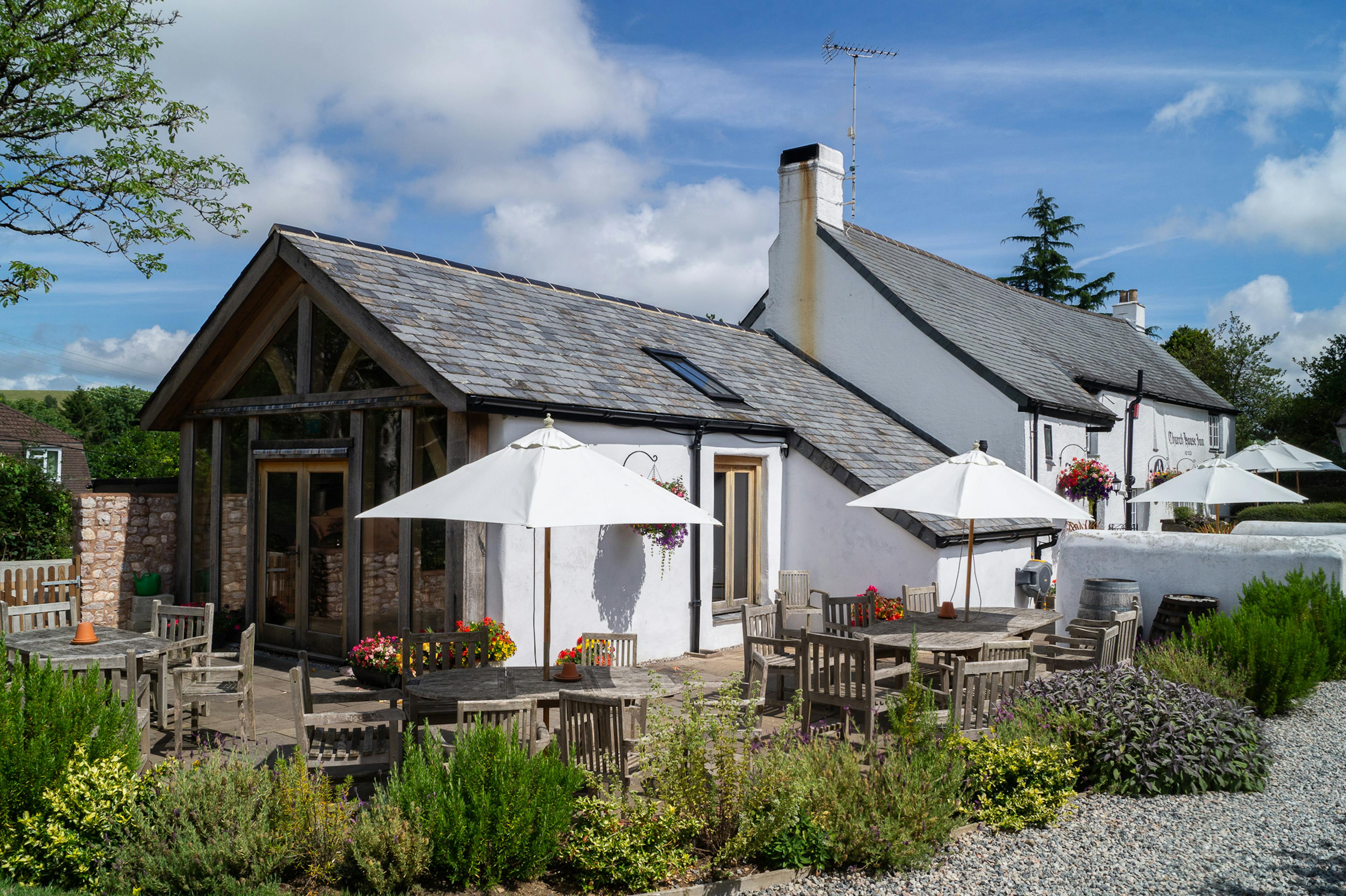 A pub garden with an oak framed extension and tables and chairs in the foreground, in the sunshine