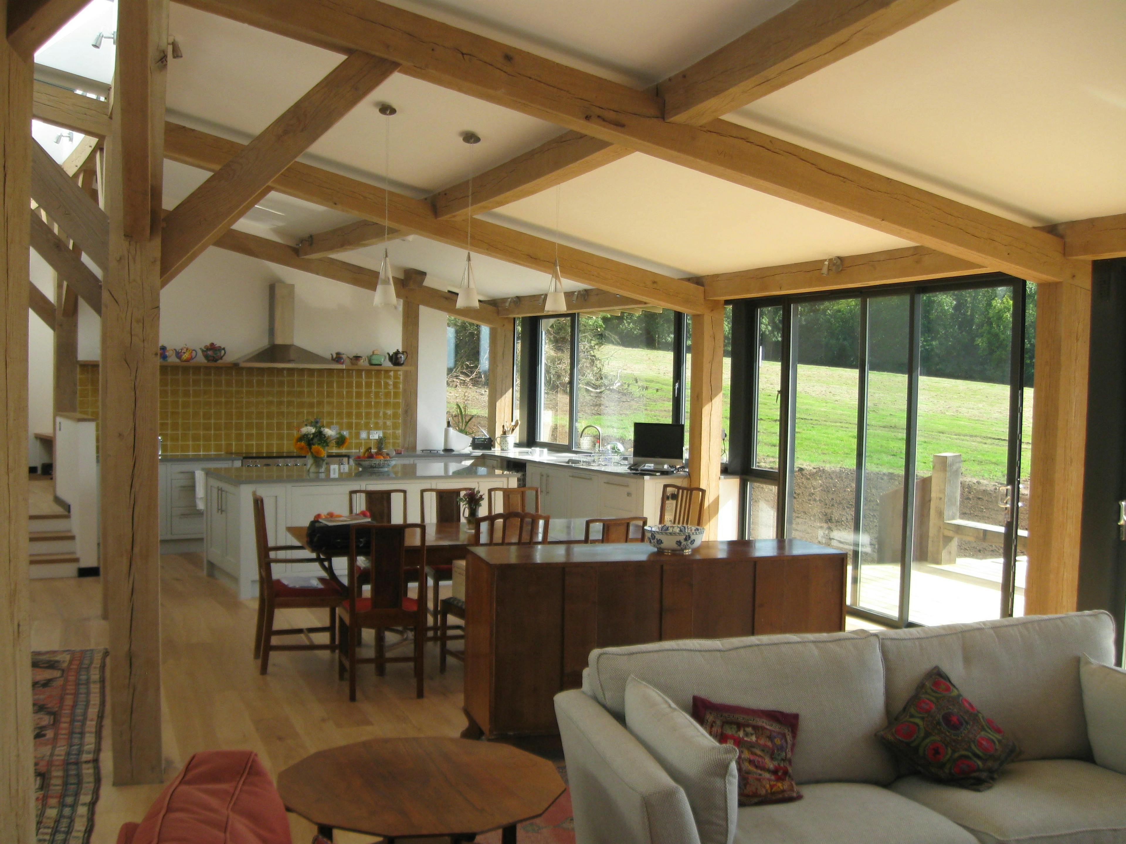 The living room of a curved oak framed house with large glazed windows, showing a sofa area, dining area and kitchen