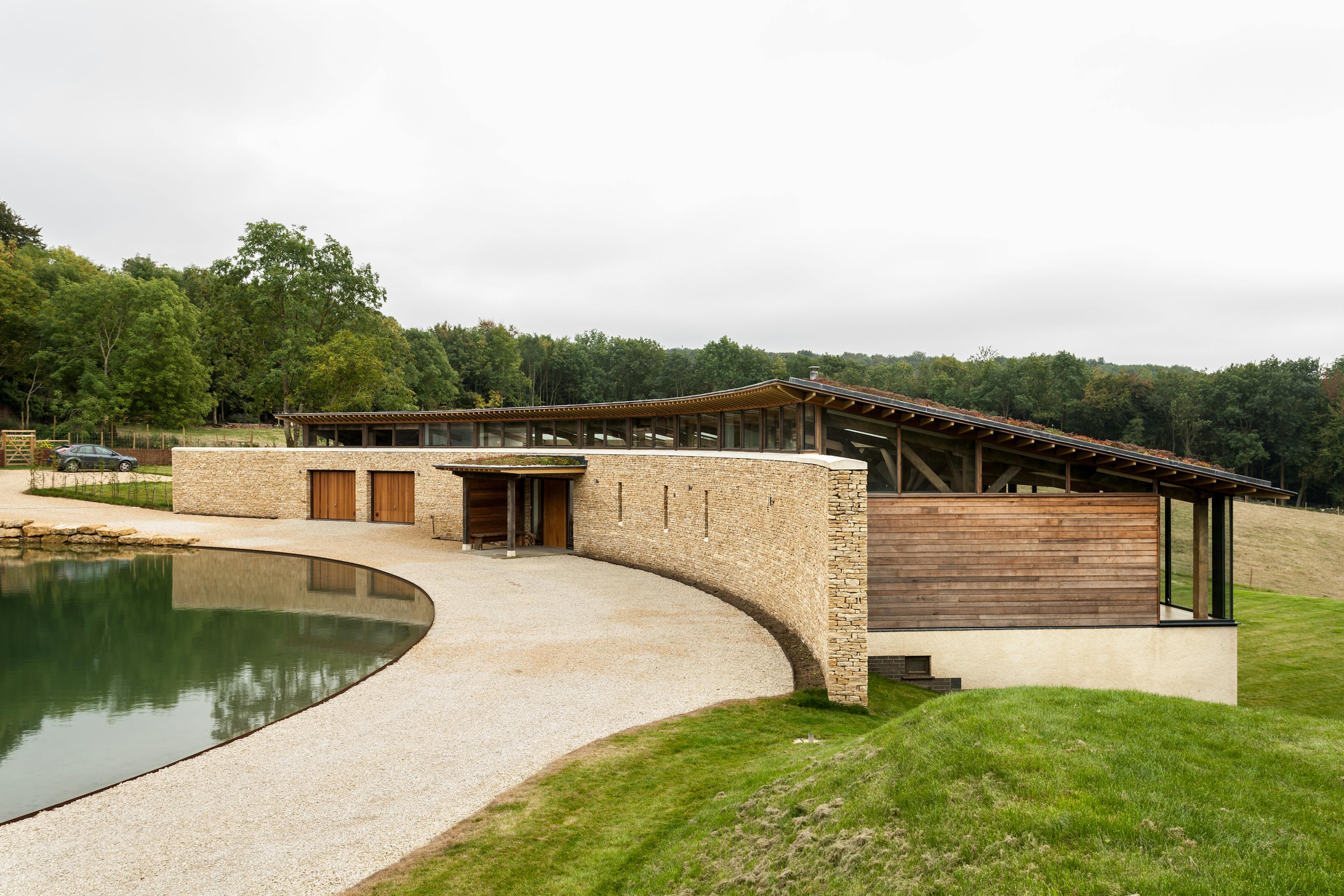 A curved oak framed house with stone finished front wall and a lake in front