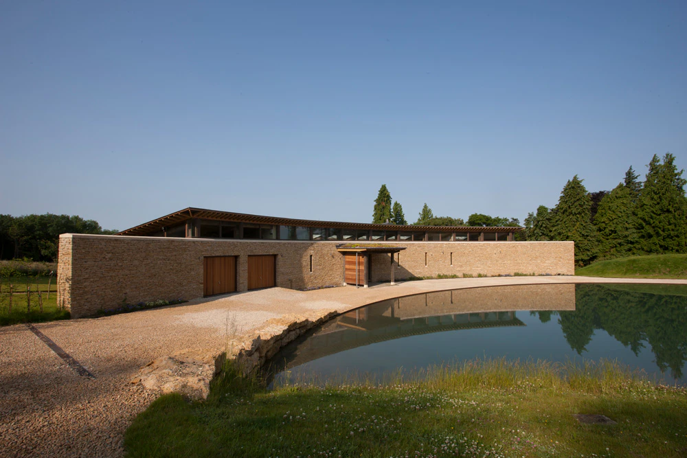 A curved oak framed house with stone finished front wall and a lake in front