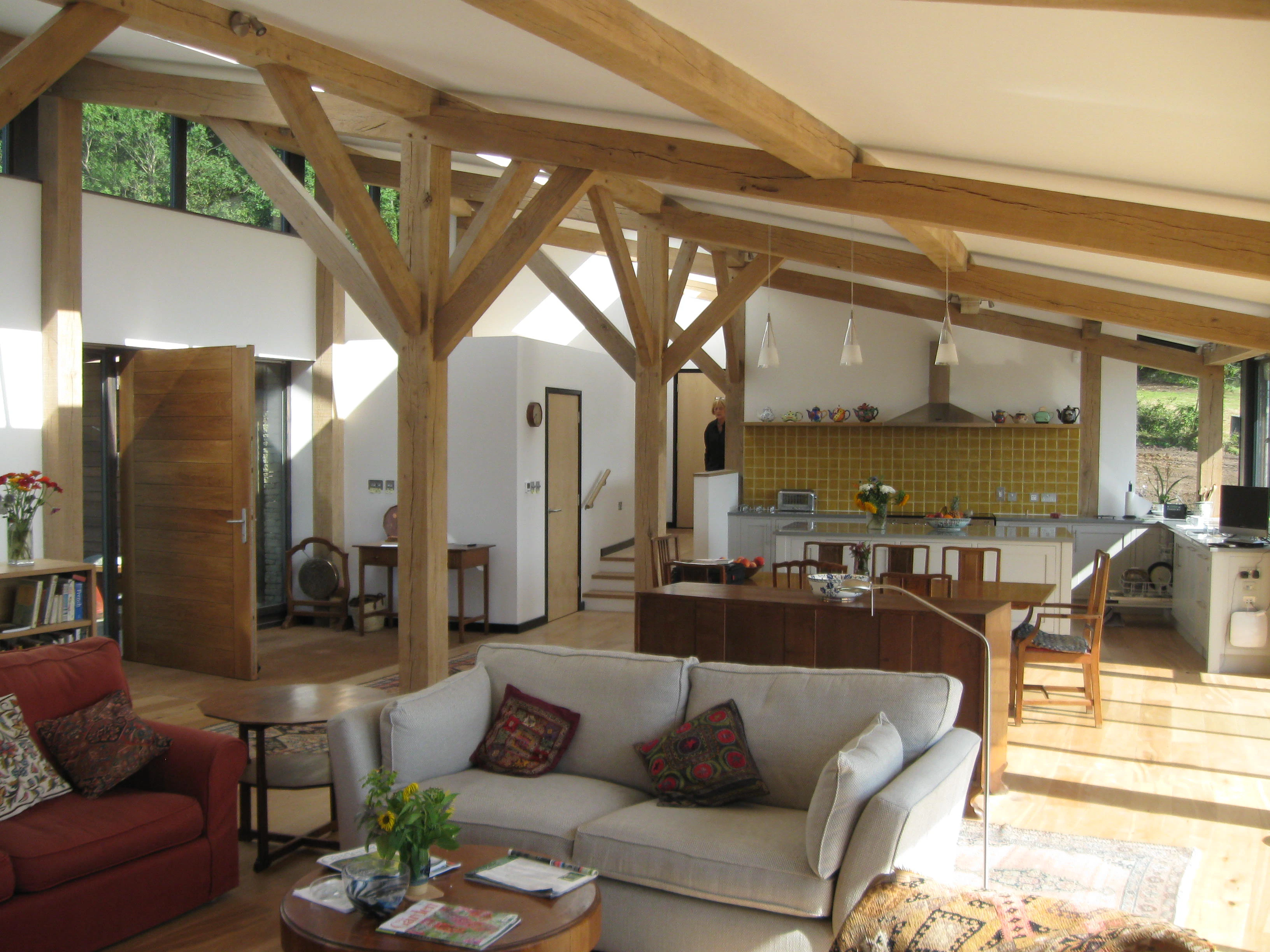 The living room of a curved oak framed house with large glazed windows, showing a sofa area, dining area and kitchen