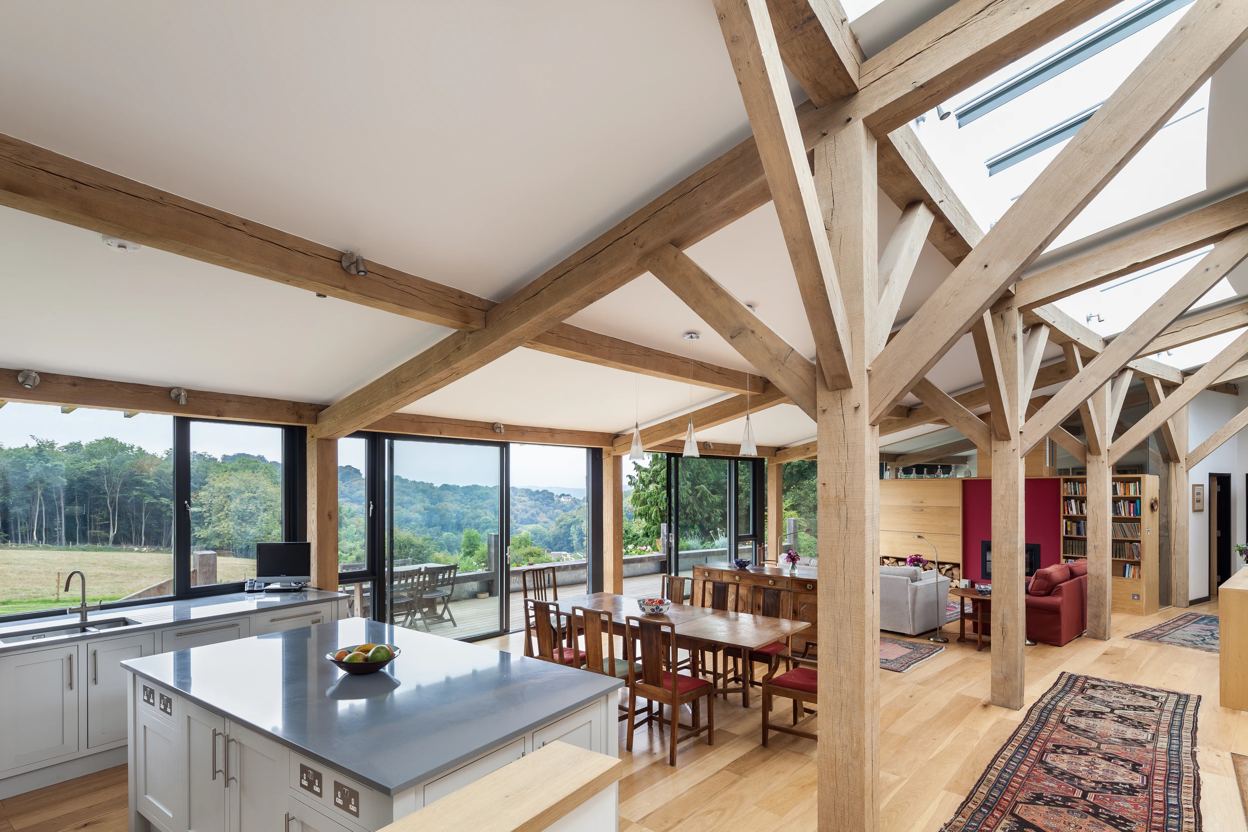 The living room of a curved oak framed house with large glazed windows, showing a kitchen, dining room and hallway