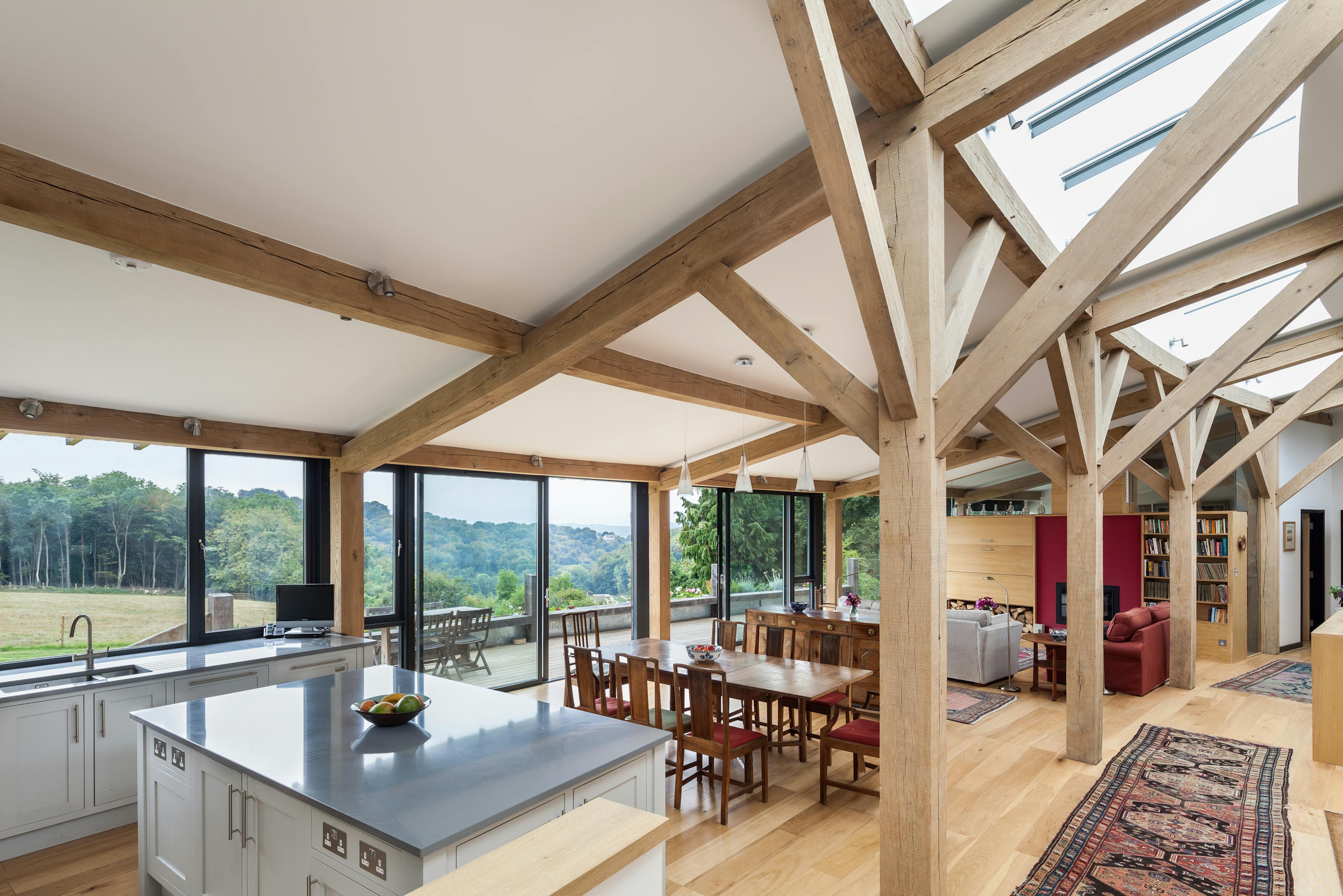The living room of a curved oak framed house with large glazed windows, showing a kitchen, dining room and hallway