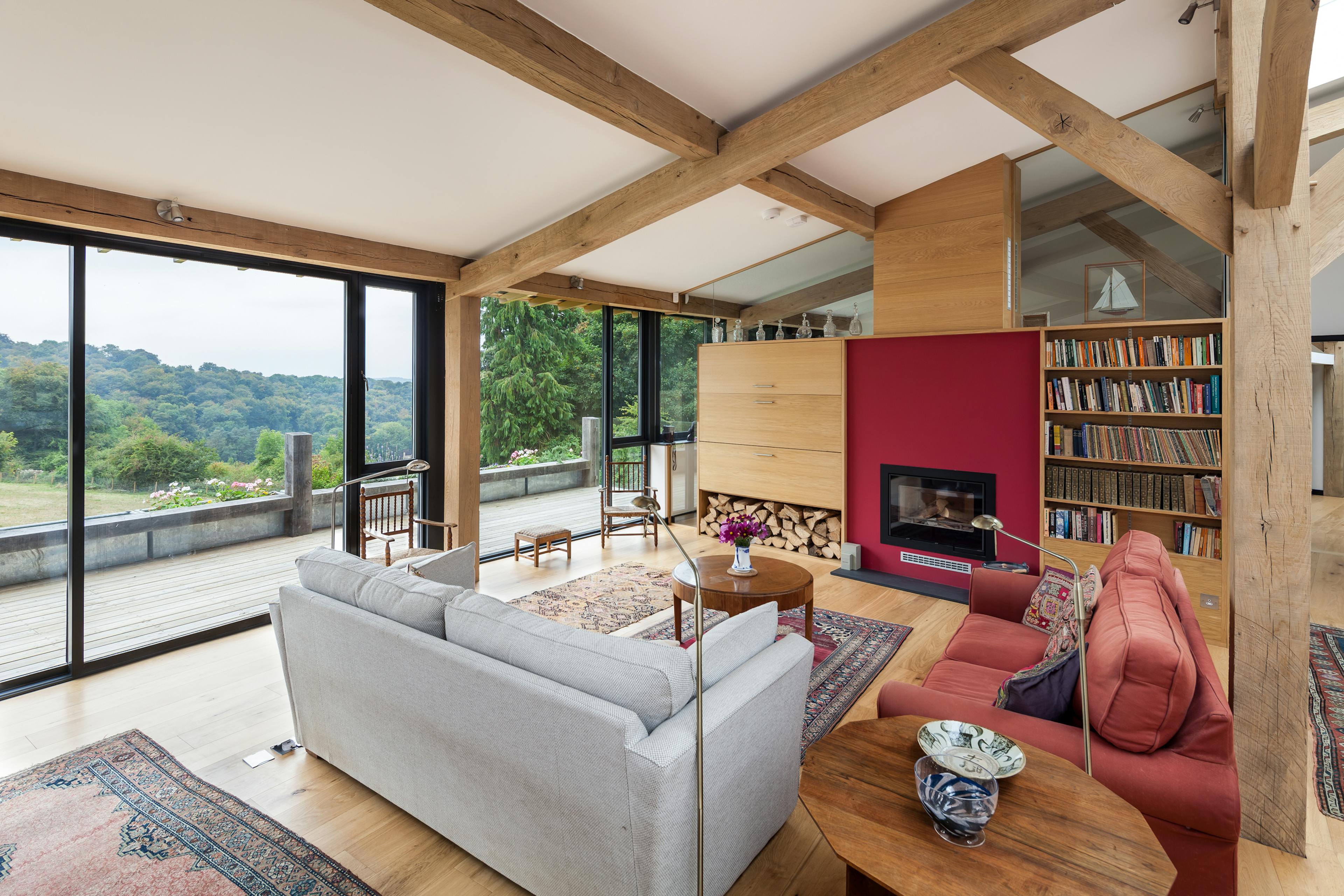The sitting room of a curved oak framed house with large glazed windows, showing a sofas and a log burner