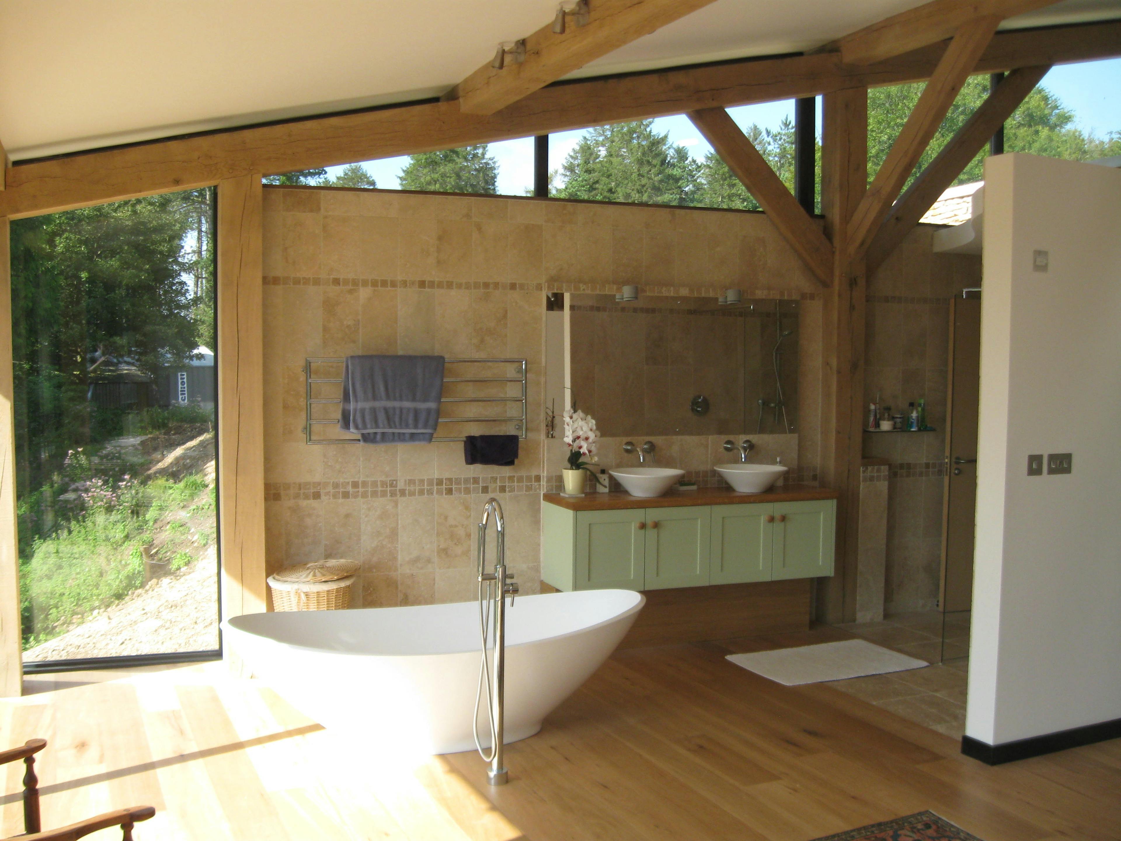 The bathroom of a curved oak framed house with a standalone bath, green cabinets and large glazed windows