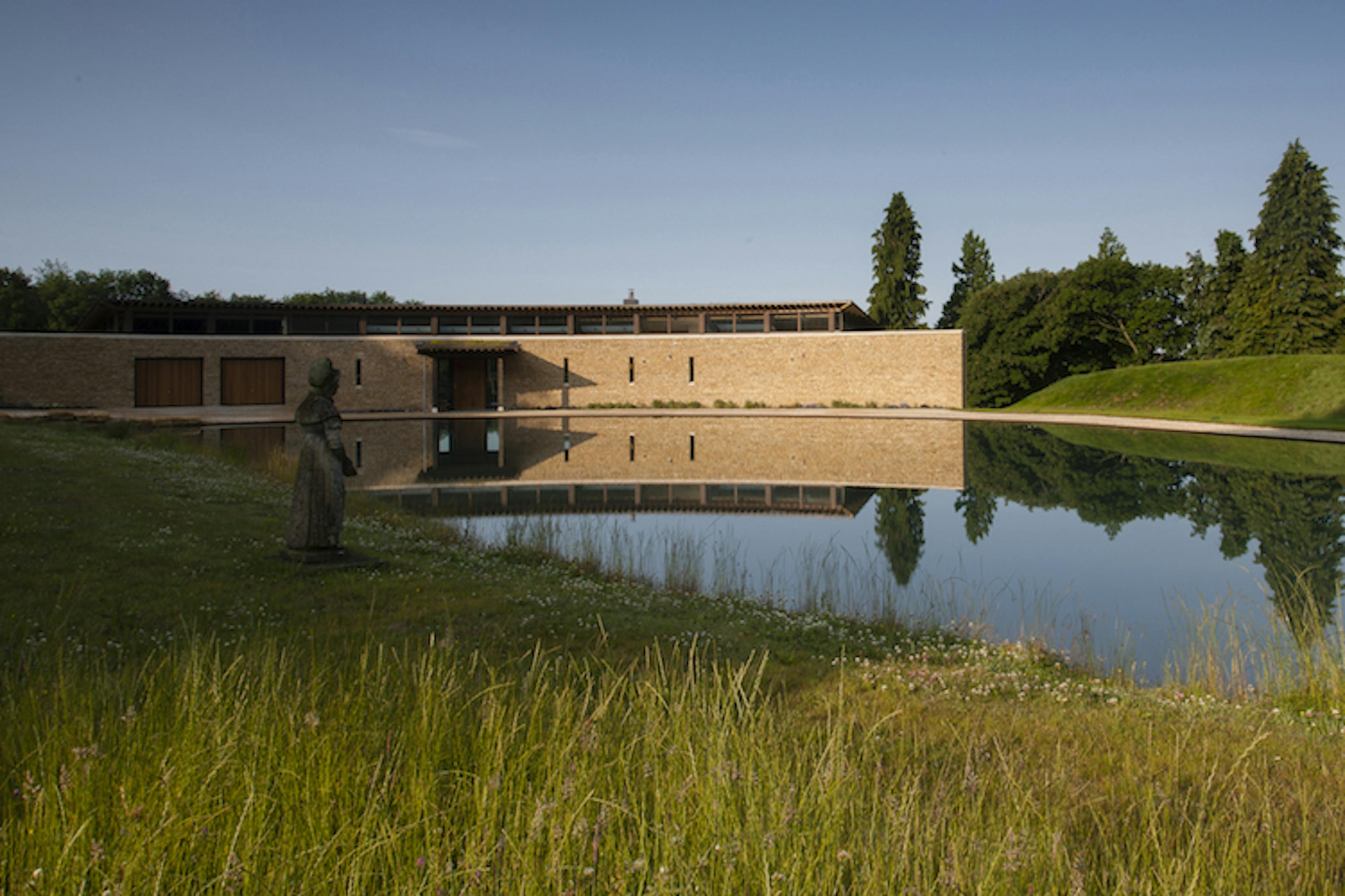 A curved oak framed house with stone finished front wall with a lake in front