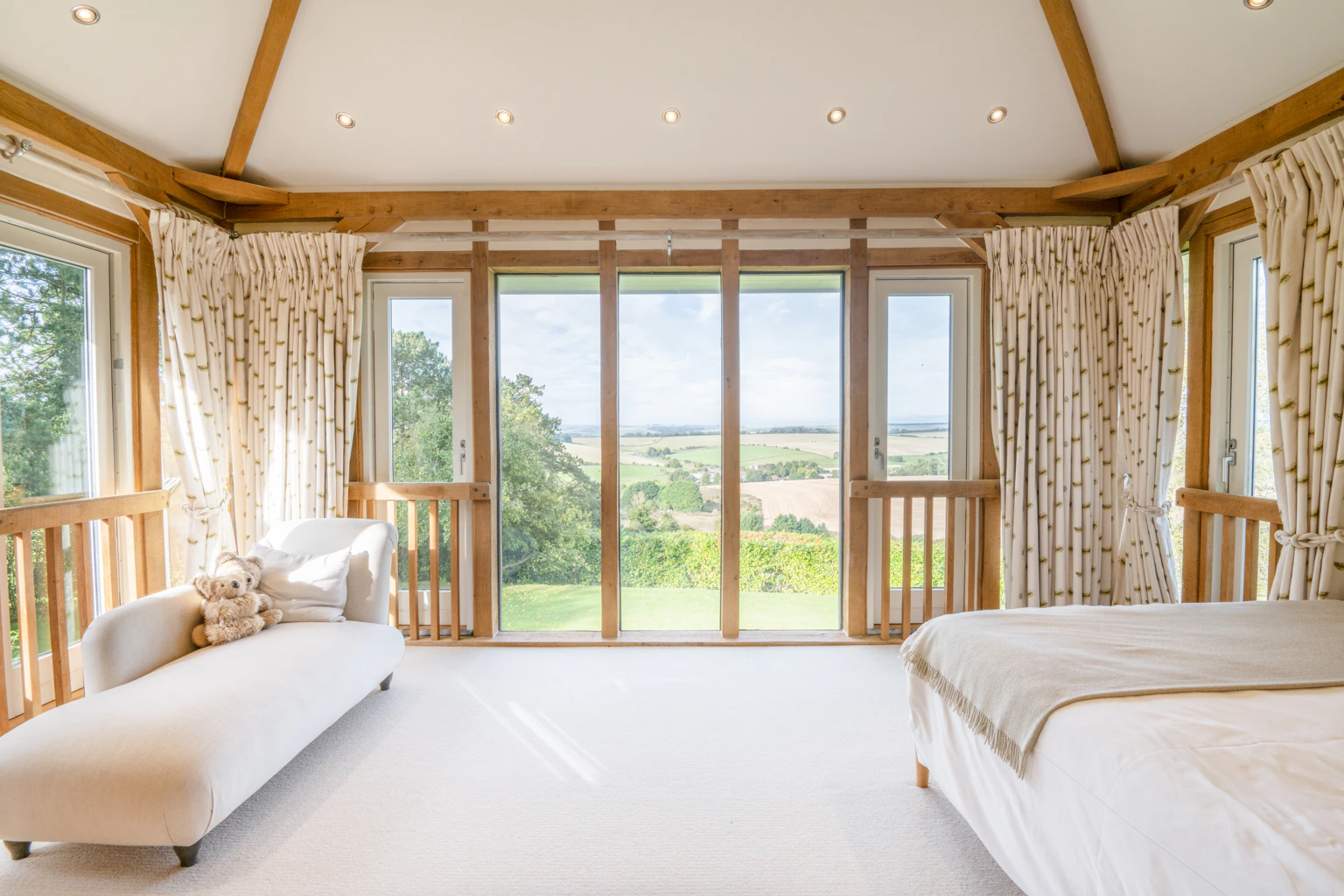 An oak framed bedroom with large glazed windows showing views of the green countryside