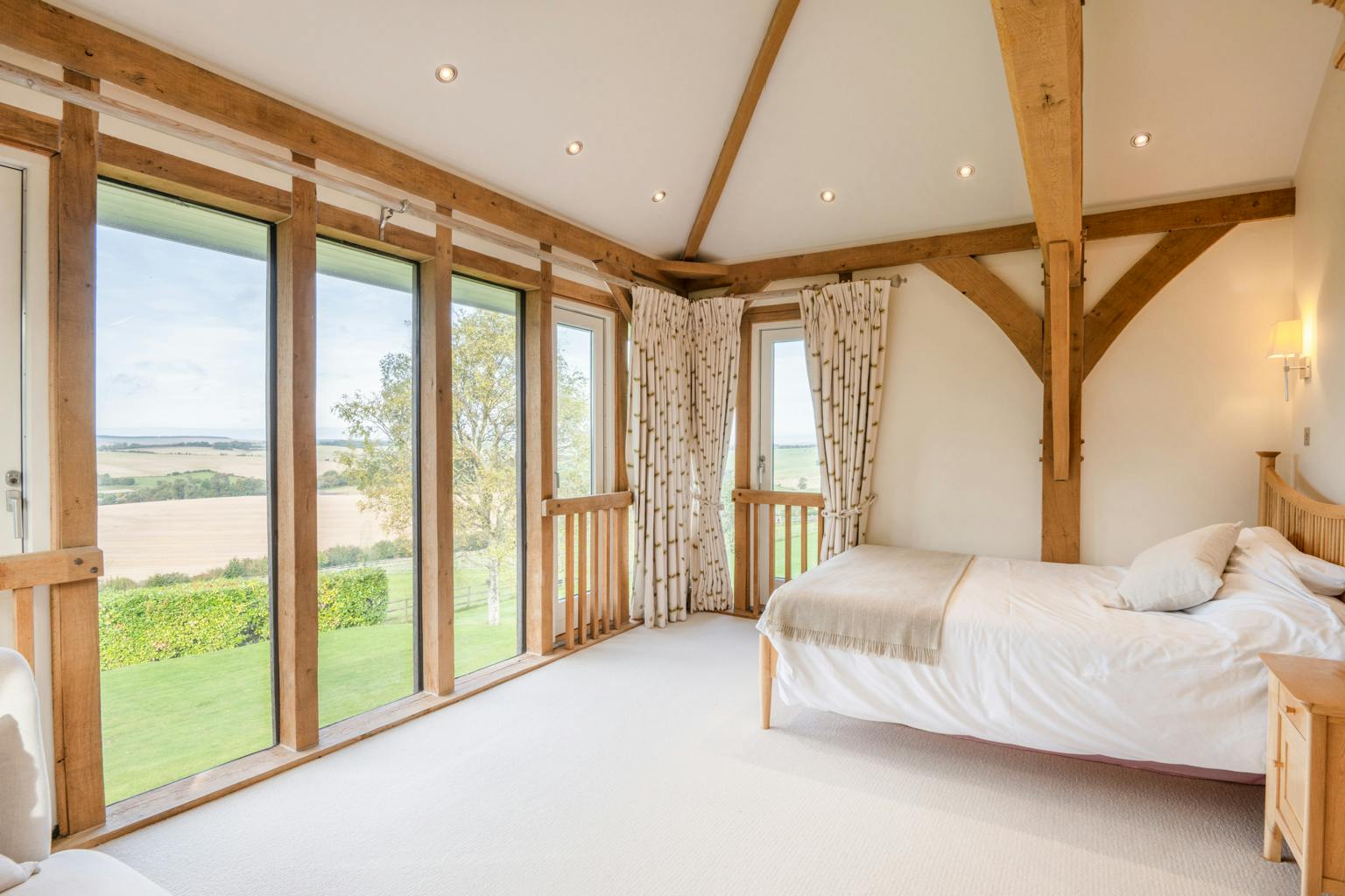 An oak framed bedroom with large glazed windows showing views of the green countryside