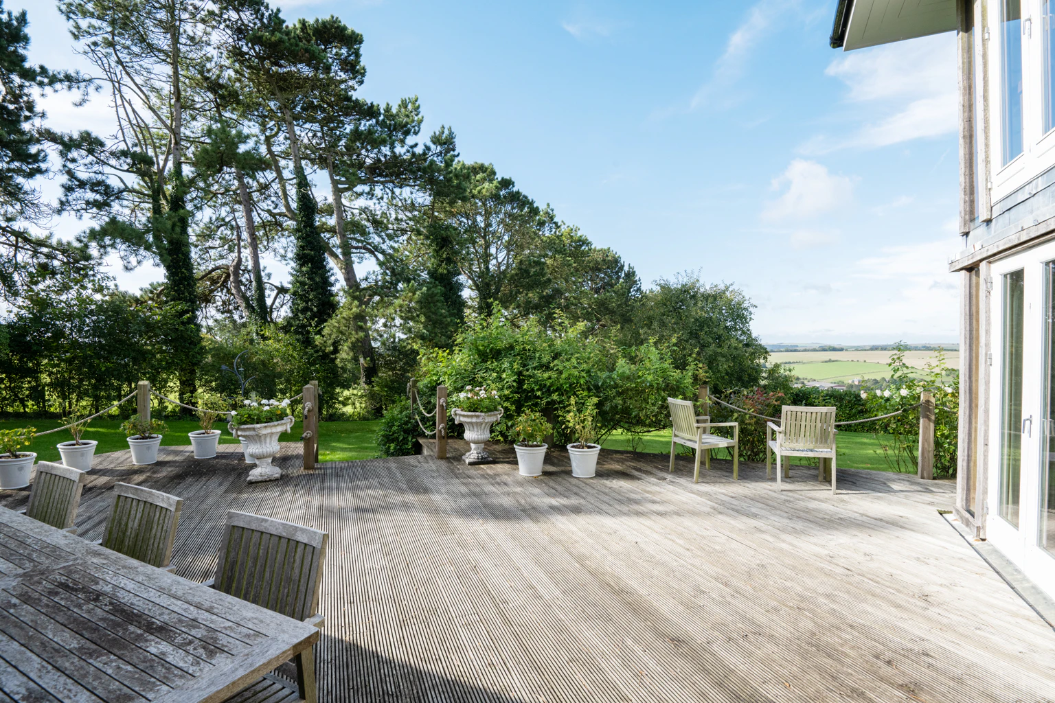 A decking area with outside table and chairs by a large home