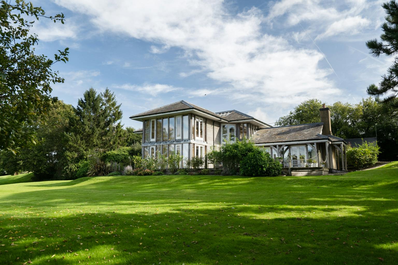 A large oak framed house with large glazed windows and a large green lawn in front