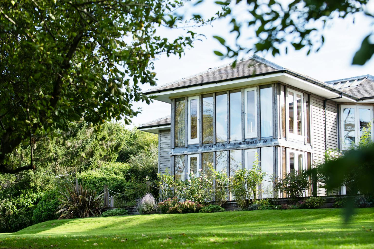 A large oak framed house with large glazed windows and a large green lawn in front