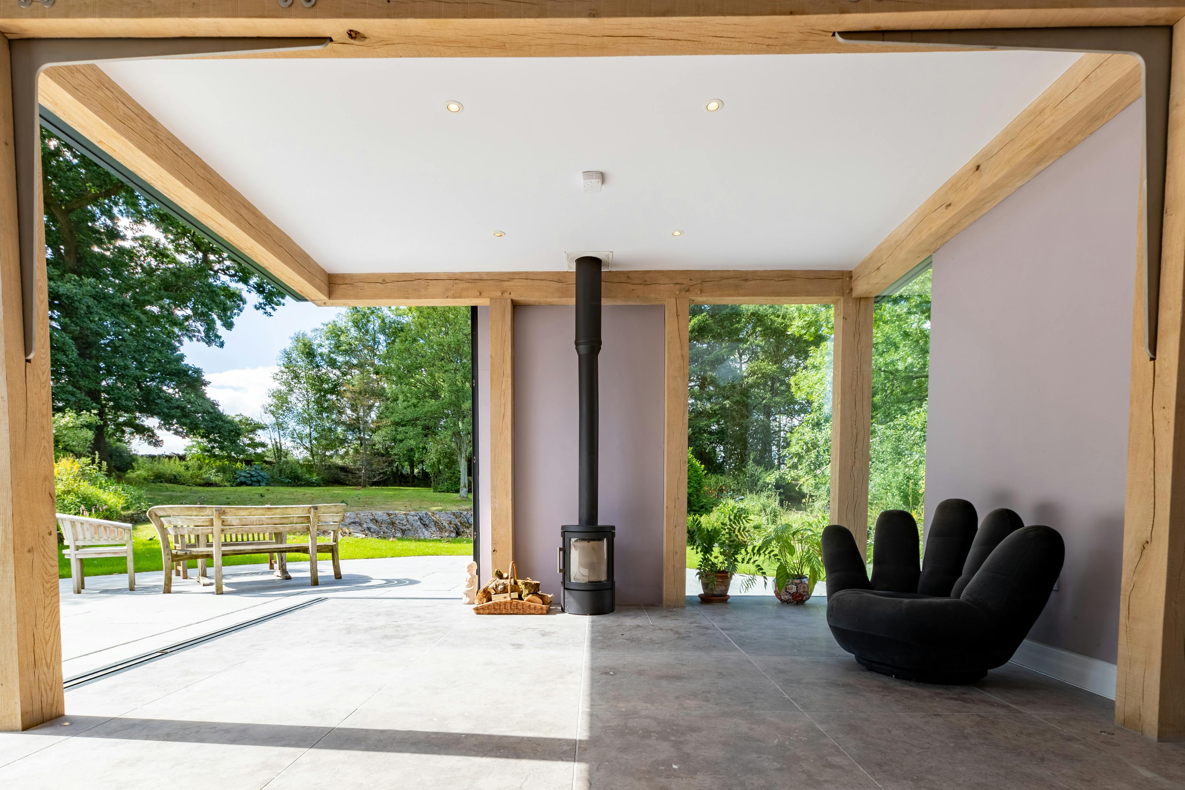 An oak frame living room extension with a log burner, showing a wide opening with direct access to a terrace and garden