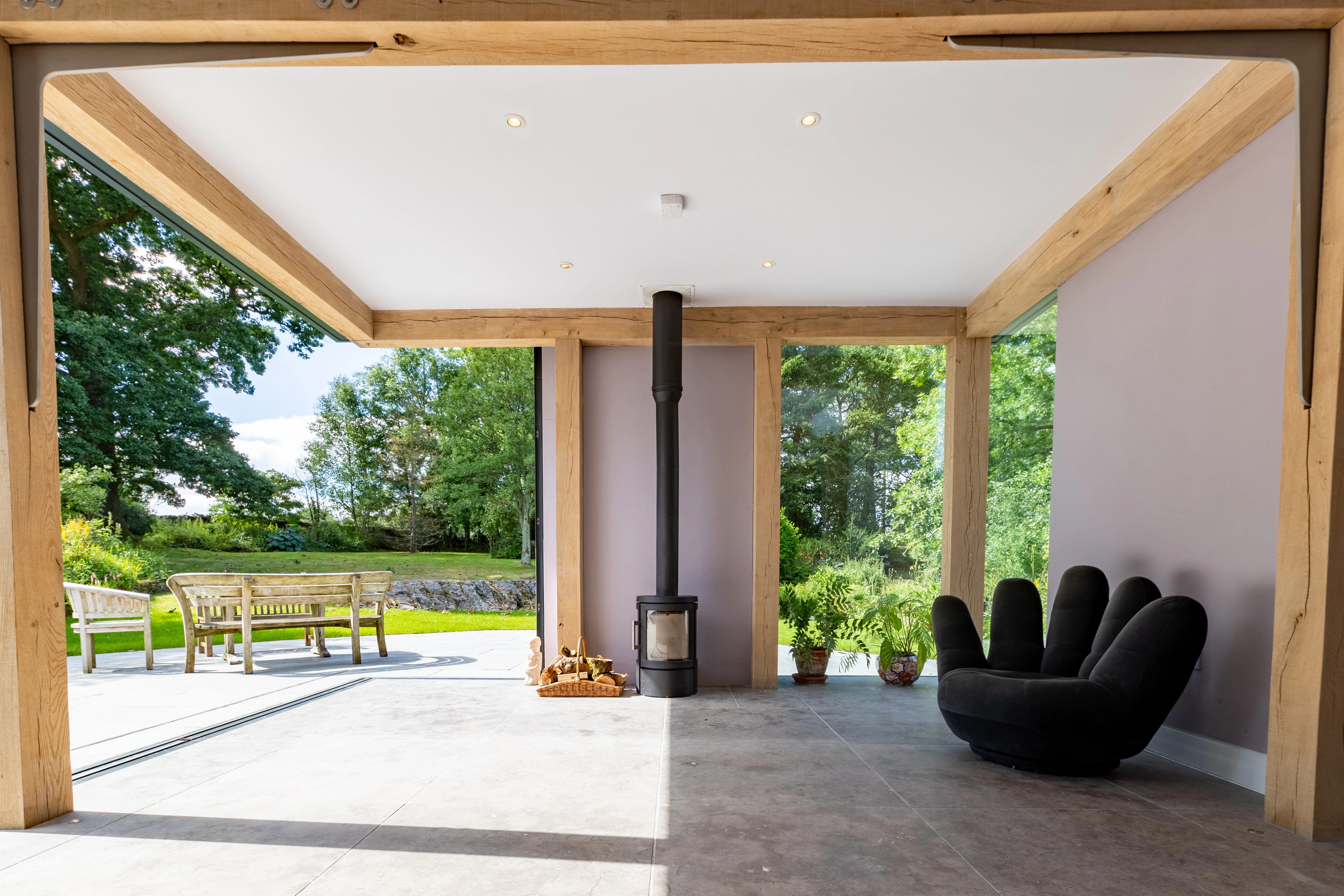 An oak frame living room extension with a log burner, showing a wide opening with direct access to a terrace and garden