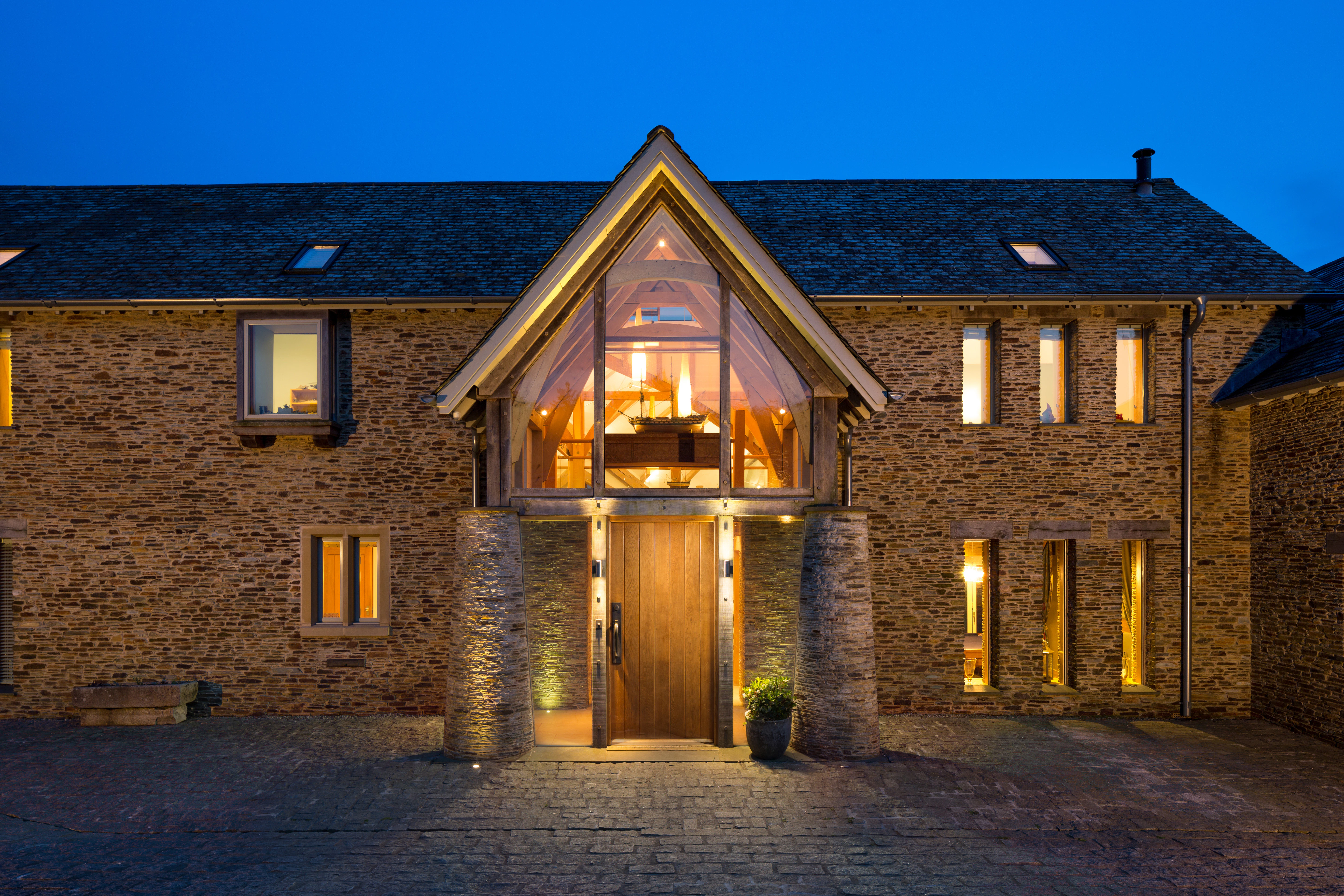 Nighttime view of an oak-framed family farmhouse featuring a double-height porch, beautifully illuminated to showcase the internal oak trusses