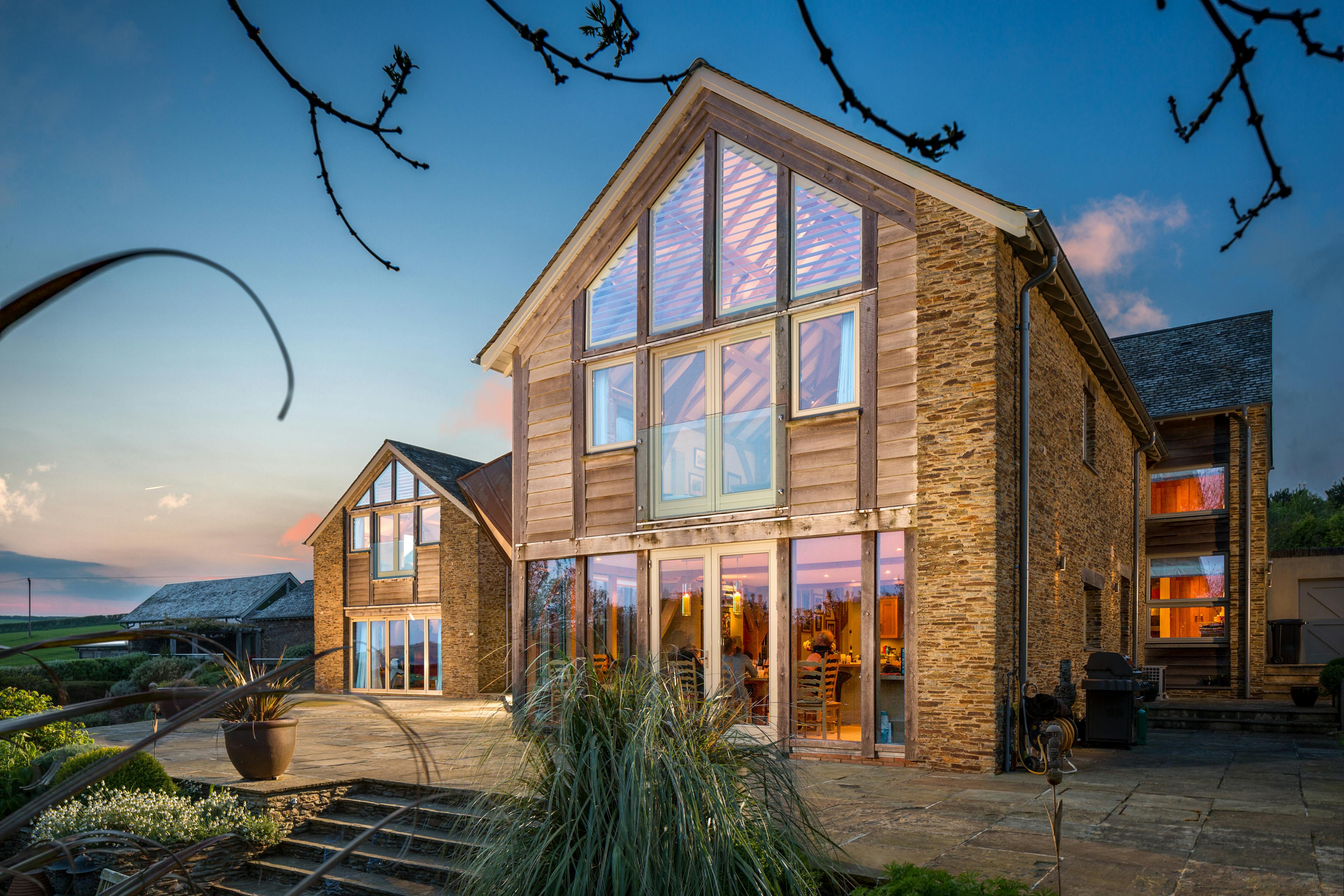 Nighttime image of a spacious two-story farmhouse-style family home, with its internal oak-frame structure beautifully illuminated