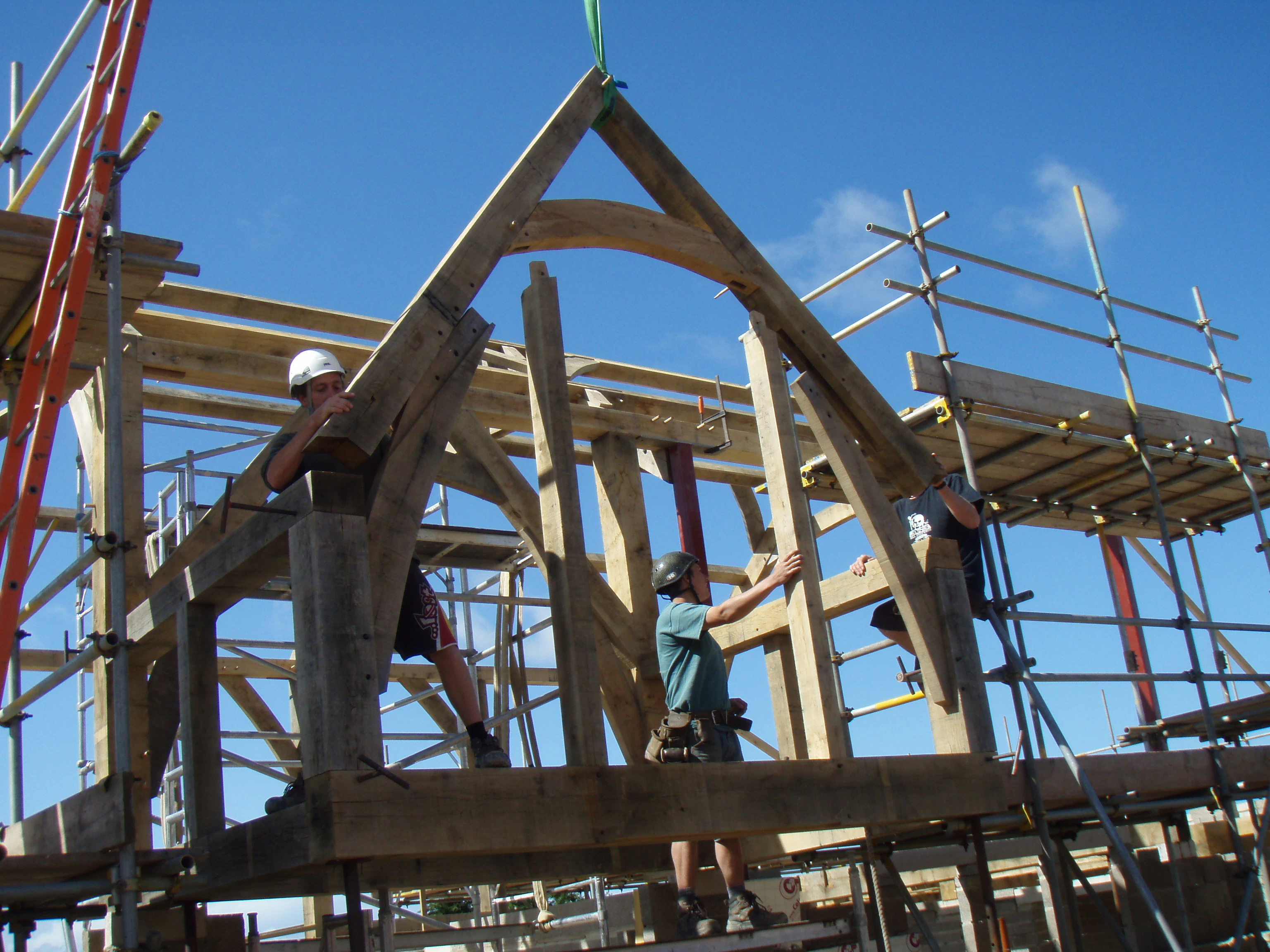 An oak sling brace and arch brace truss for the front two-story porch being lifted into place at the construction site