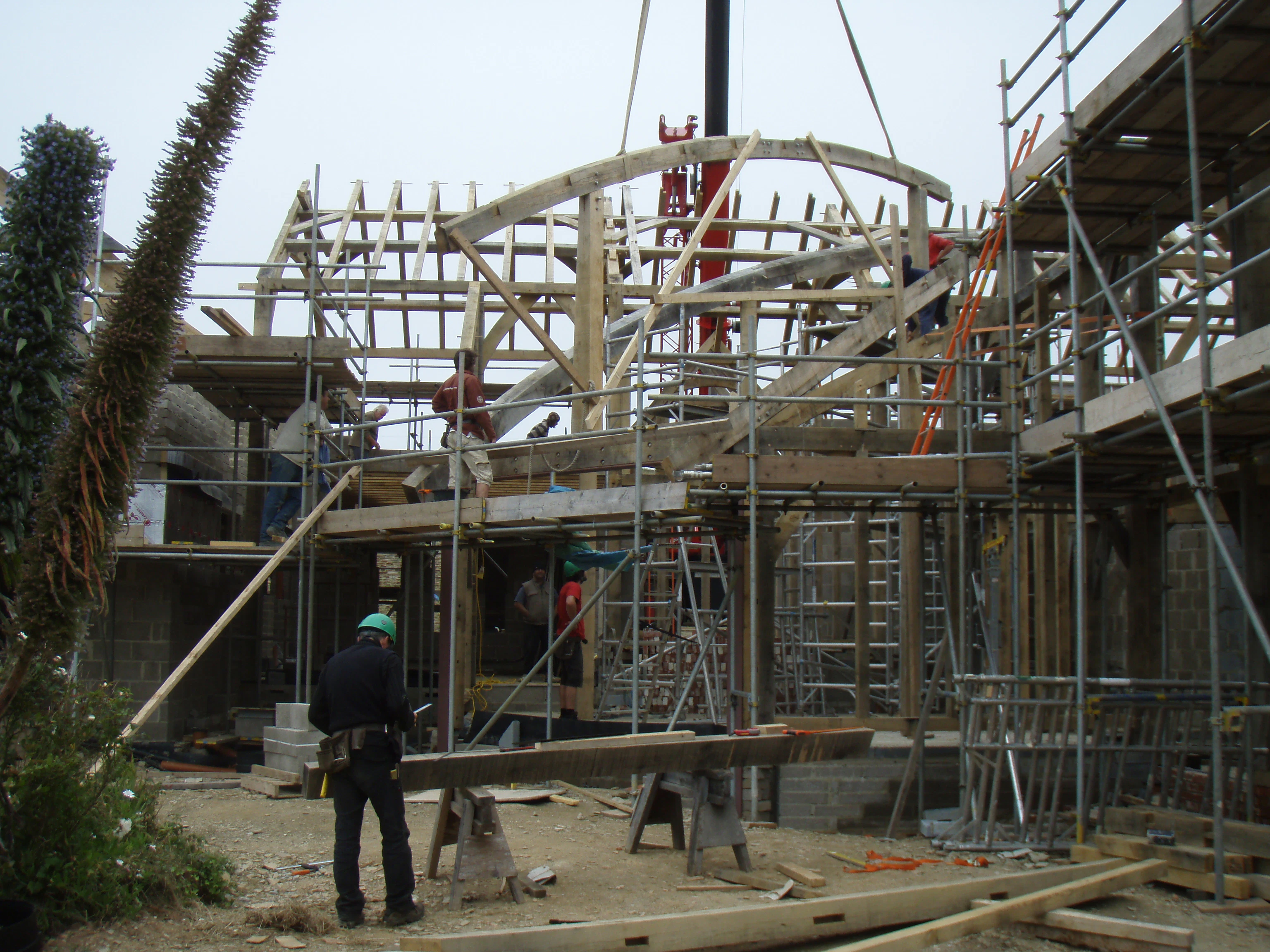 Initial stages of assembling the boat roof structure, with curved oak beams being lowered into place using a crane on-site