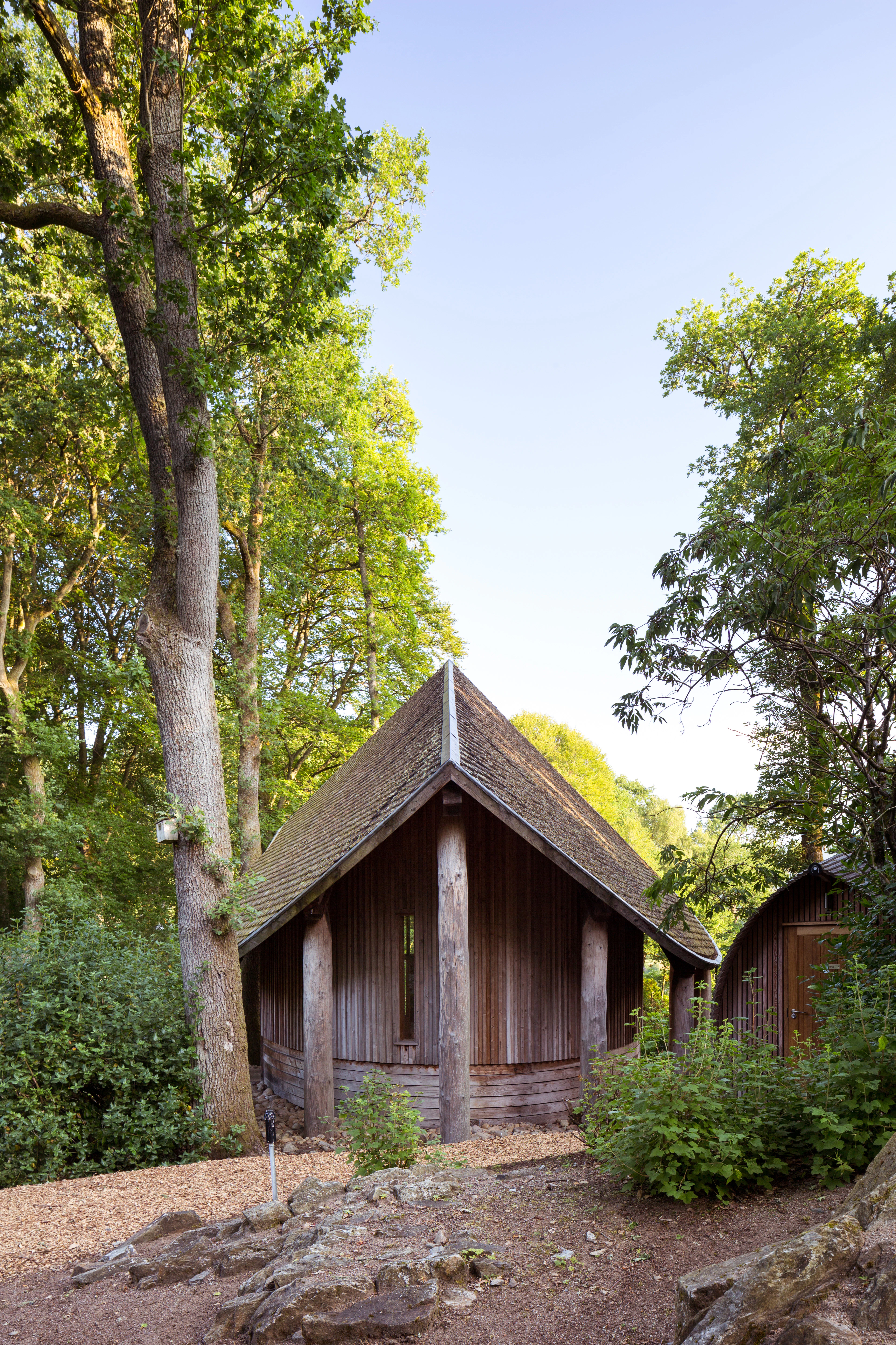 A wooden pavilion with a shingled angled roof can be seen between trees