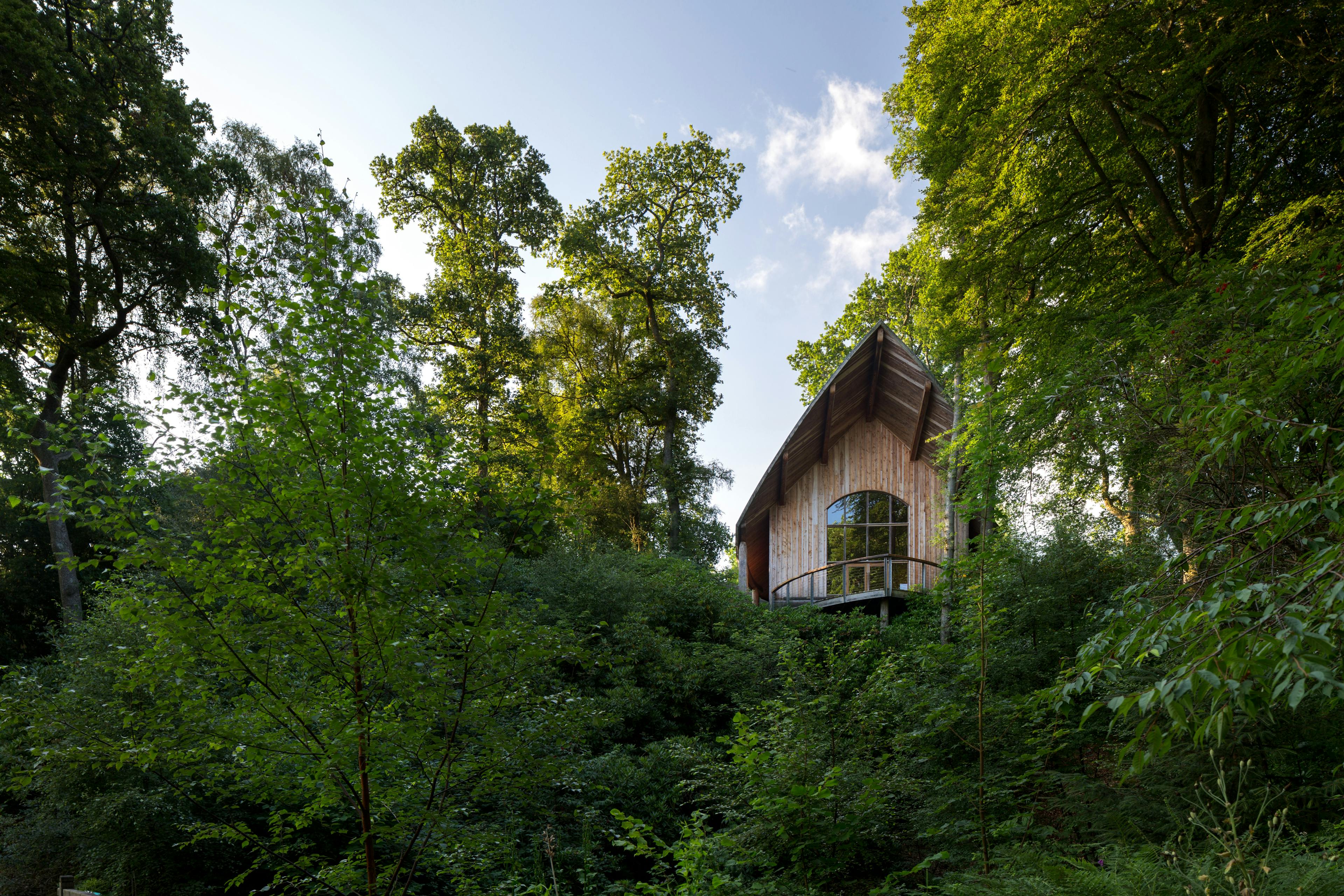A wooden pavilion with an angled roof and a balcony can be seen between trees
