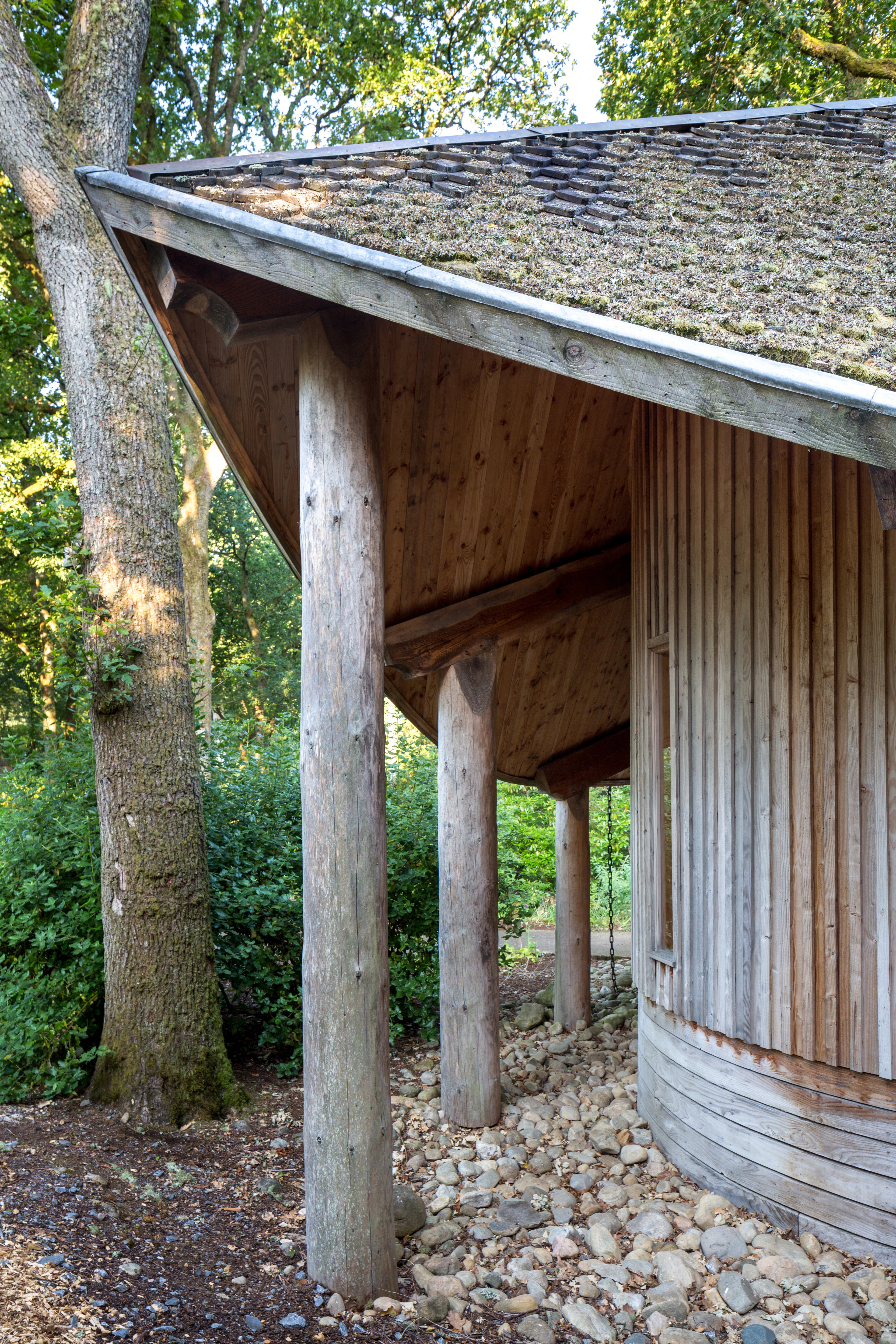 A wooden pavilion with an angled roof in a forest