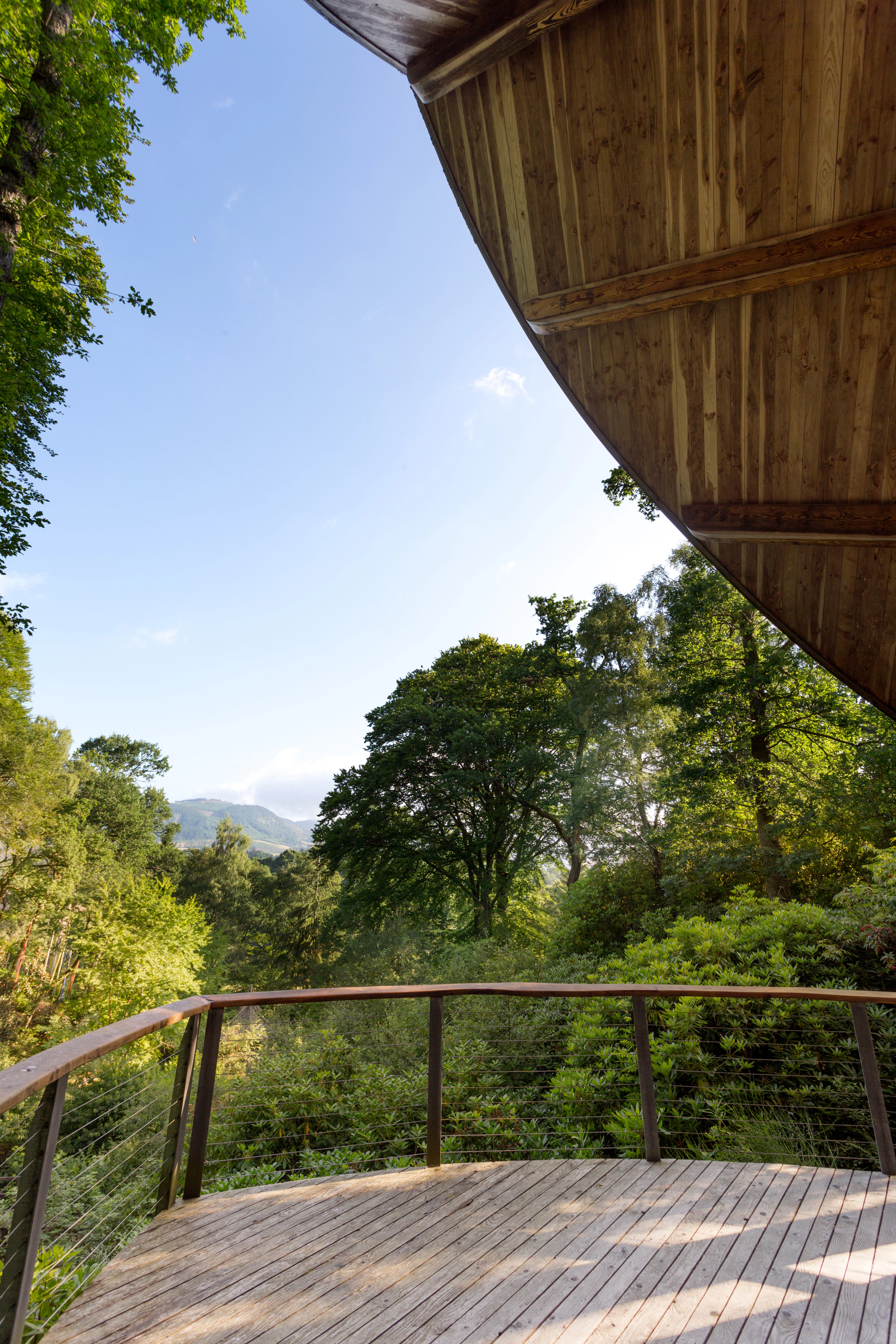 A wooden pavilion with an angled roof and wooden balcony overlooking a forest and distant views