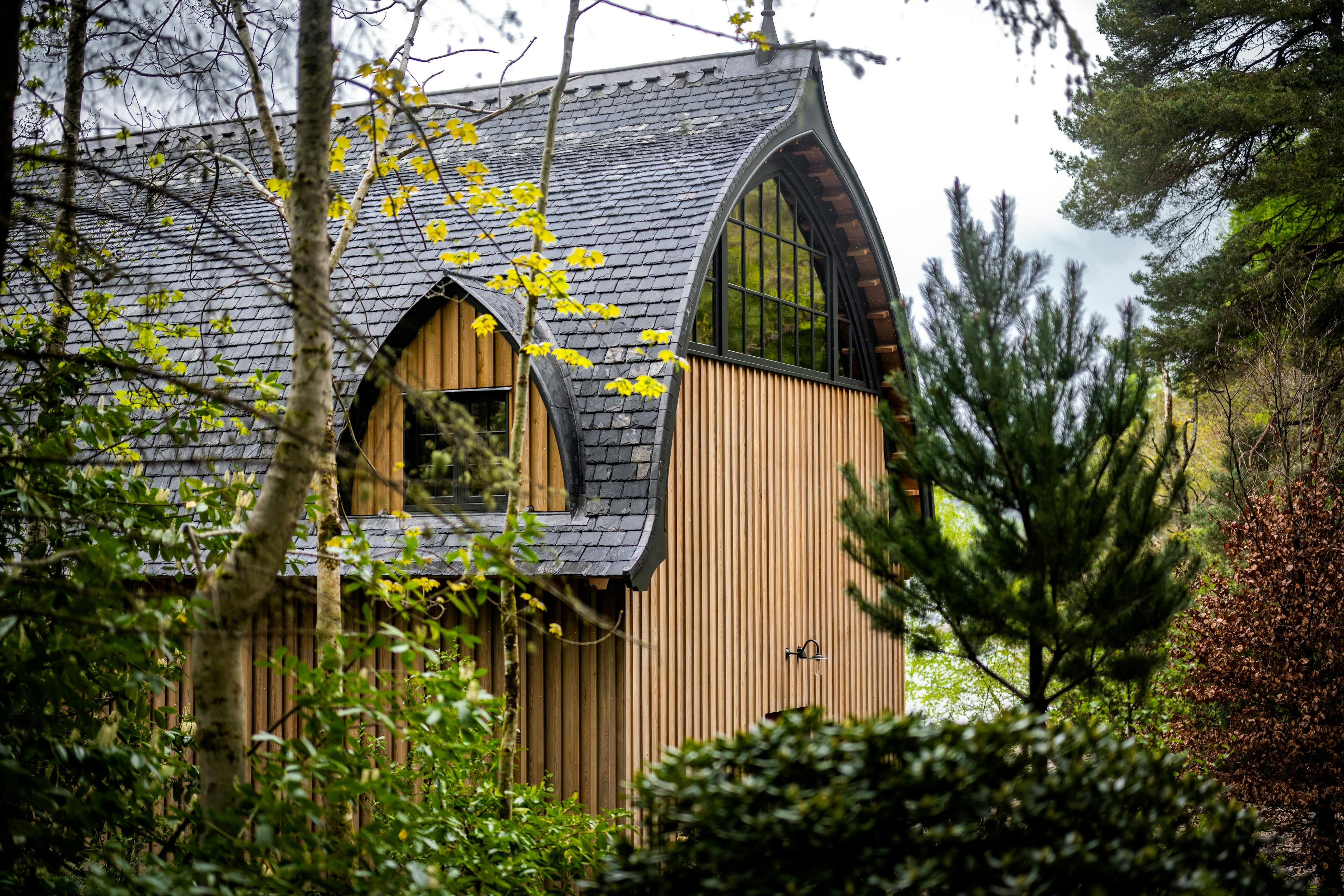 The back of a timber framed boathouse with larch cladding on loch ness with a curved roof