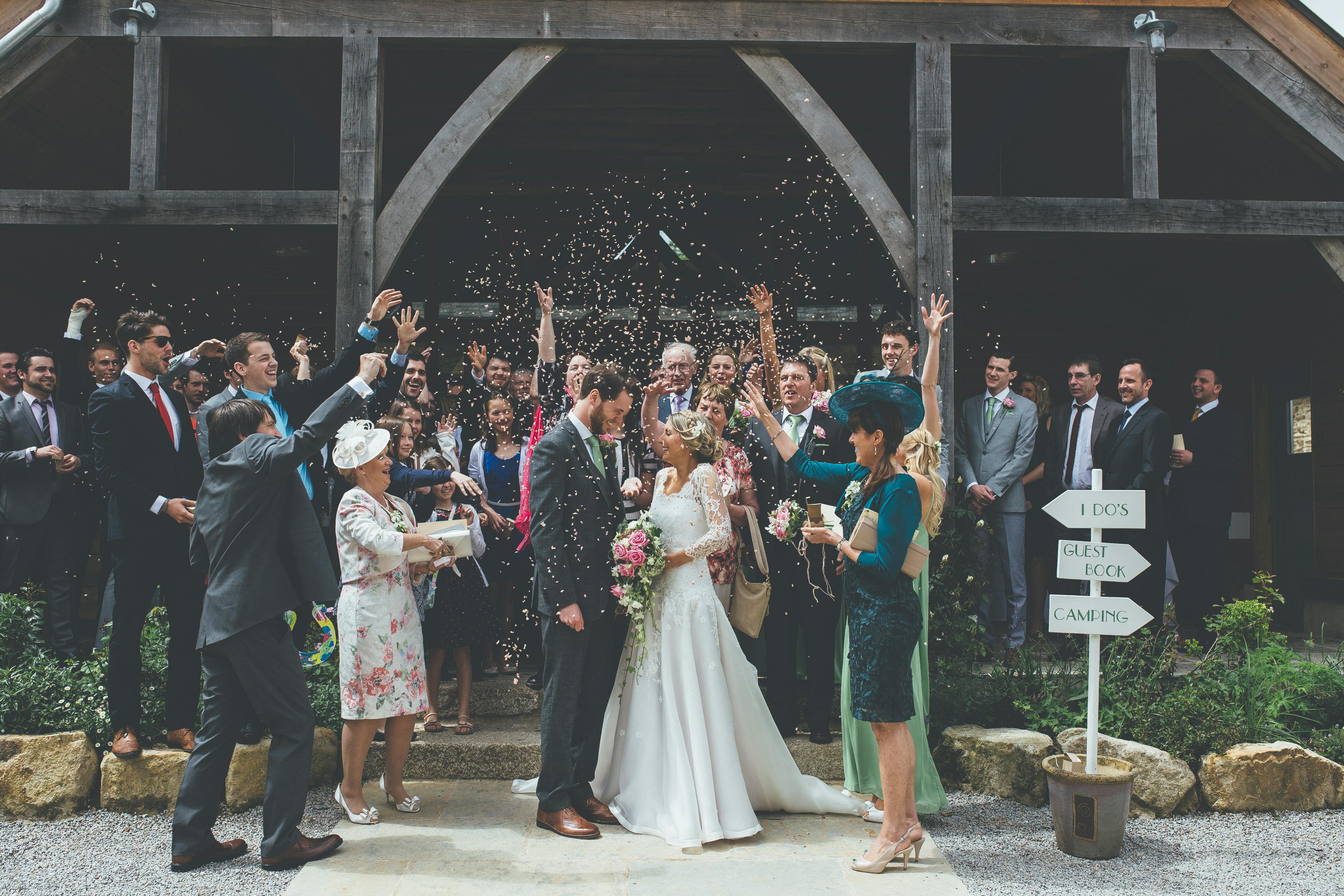 A bride and groom and wedding guests at a wedding outside an oak framed wedding barn