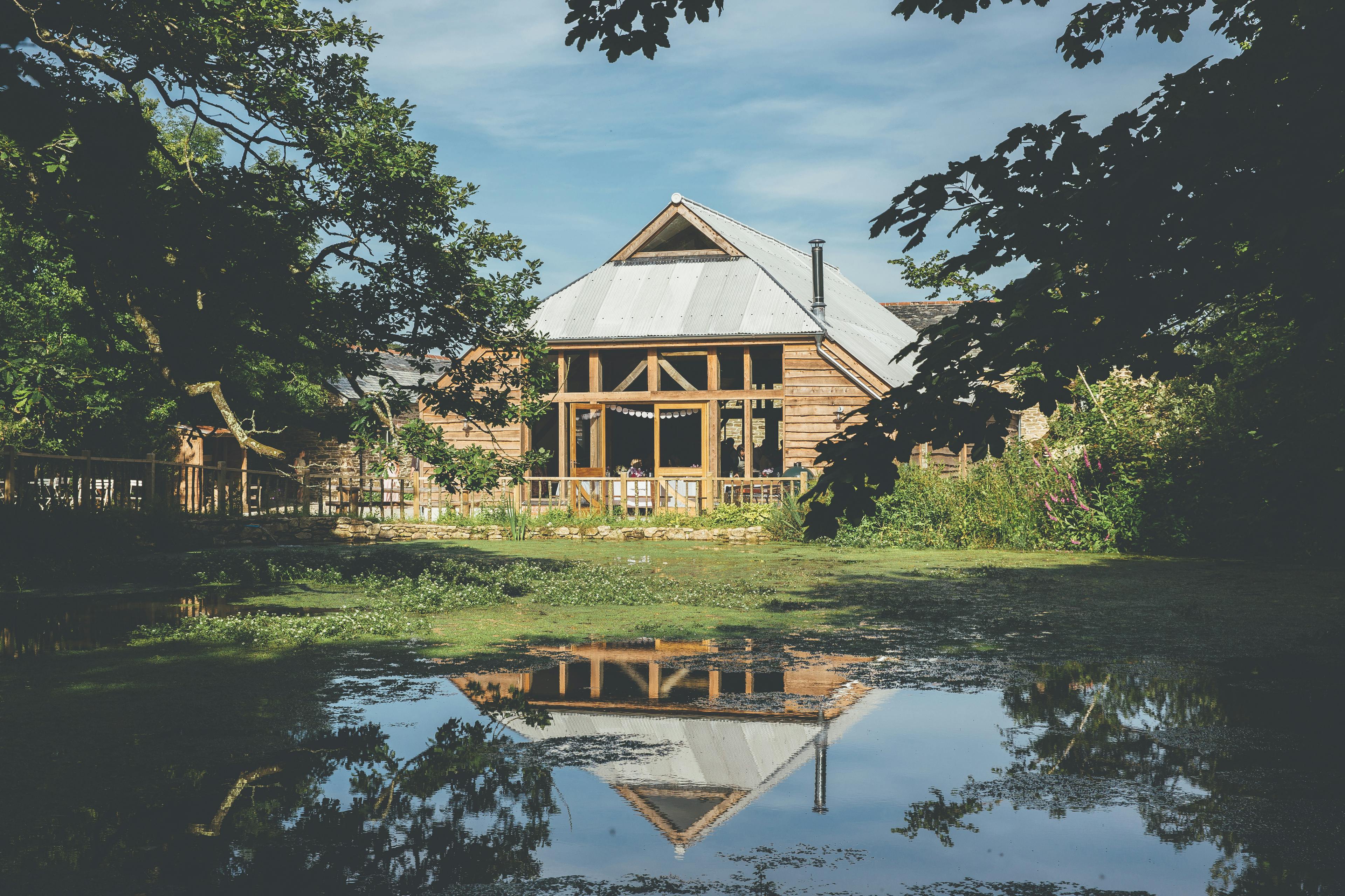 An oak framed wedding barn with a lake in front of it which reflects an image of the building