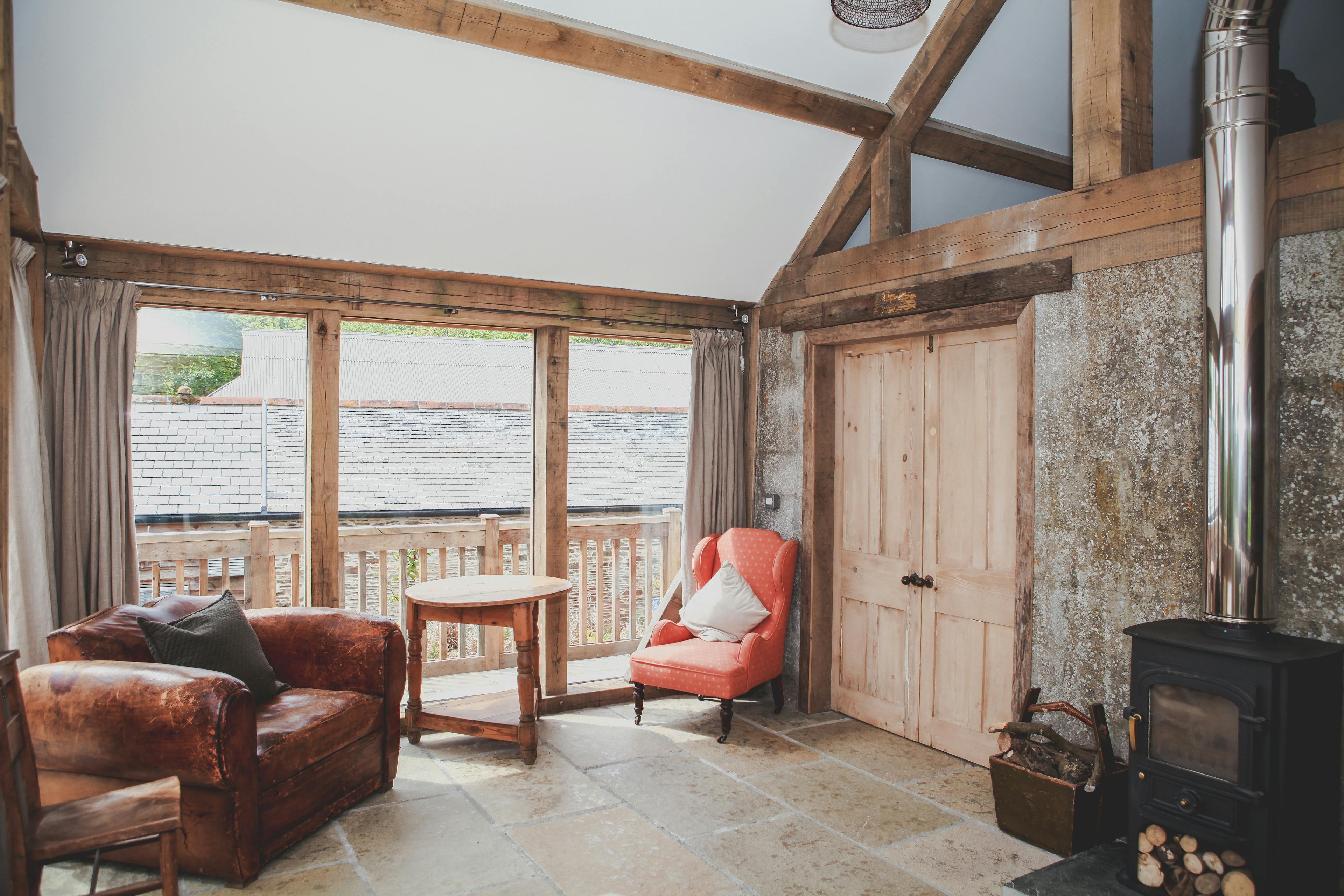A log burner and leather armchair inside an oak framed cabin with a direct glazing