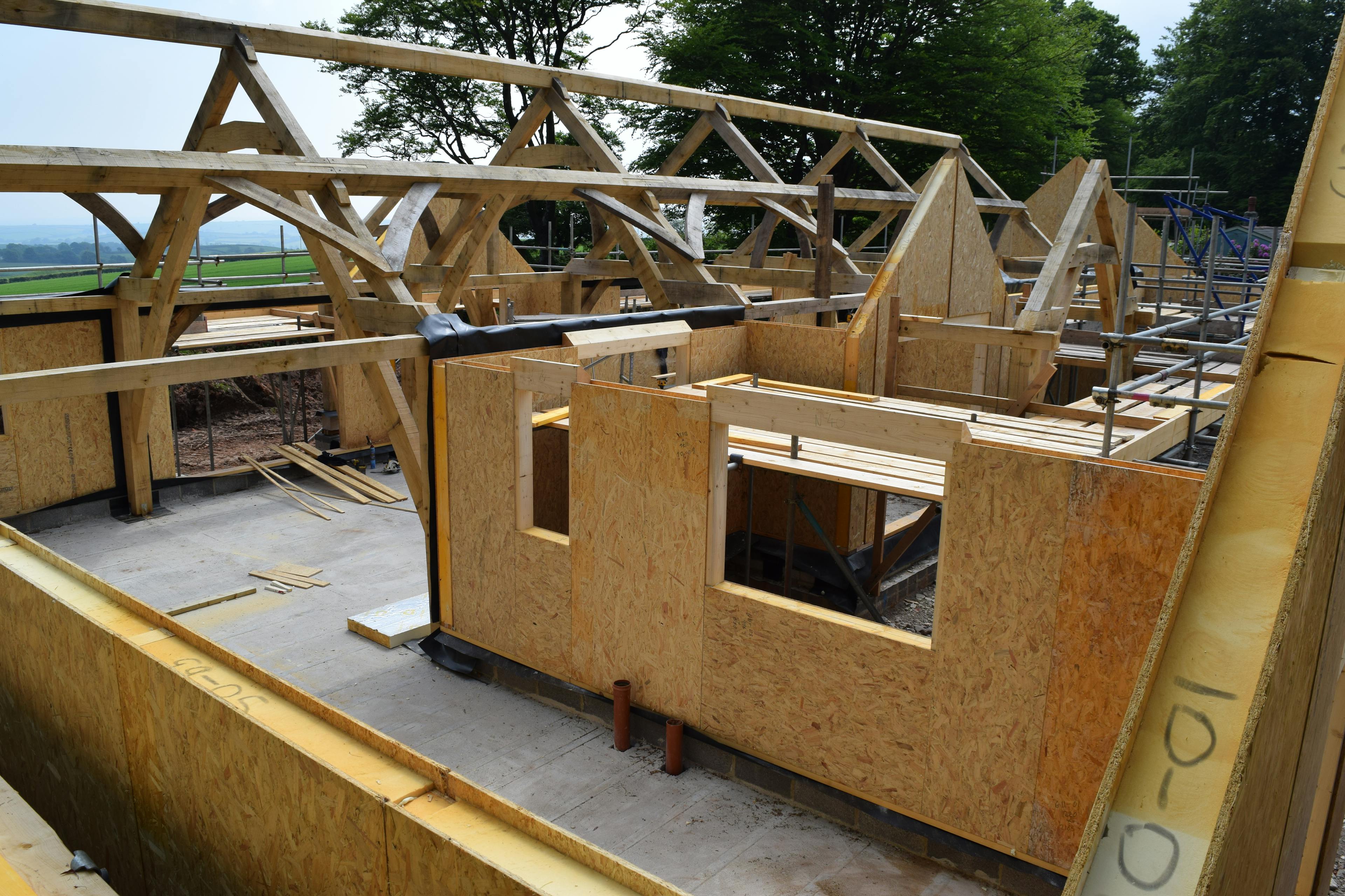 On a construction site an oak frame being wrapped in SIPs structurally insulated panels