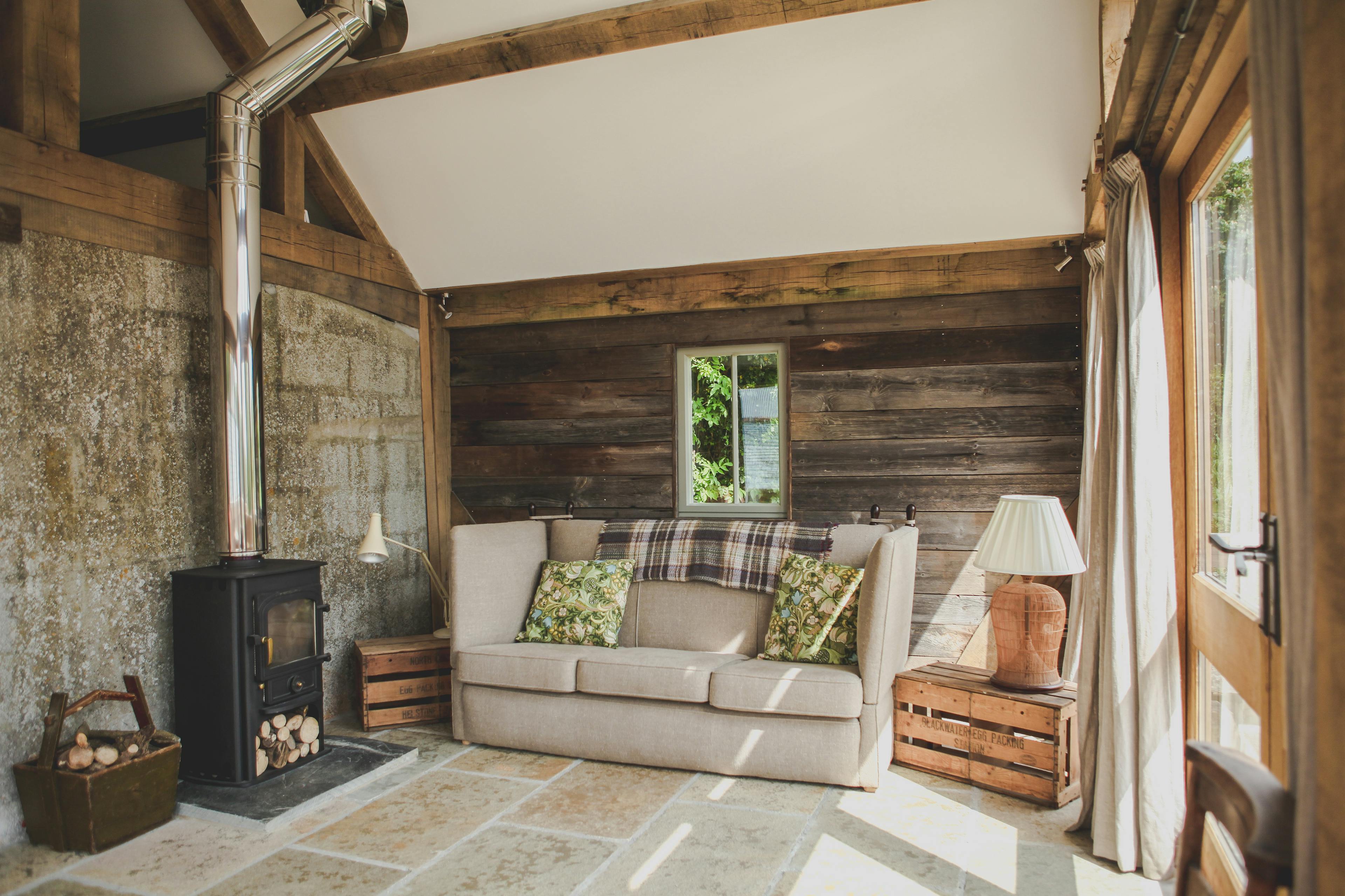 A log burner and sofa inside an oak framed cabin with a direct glazing