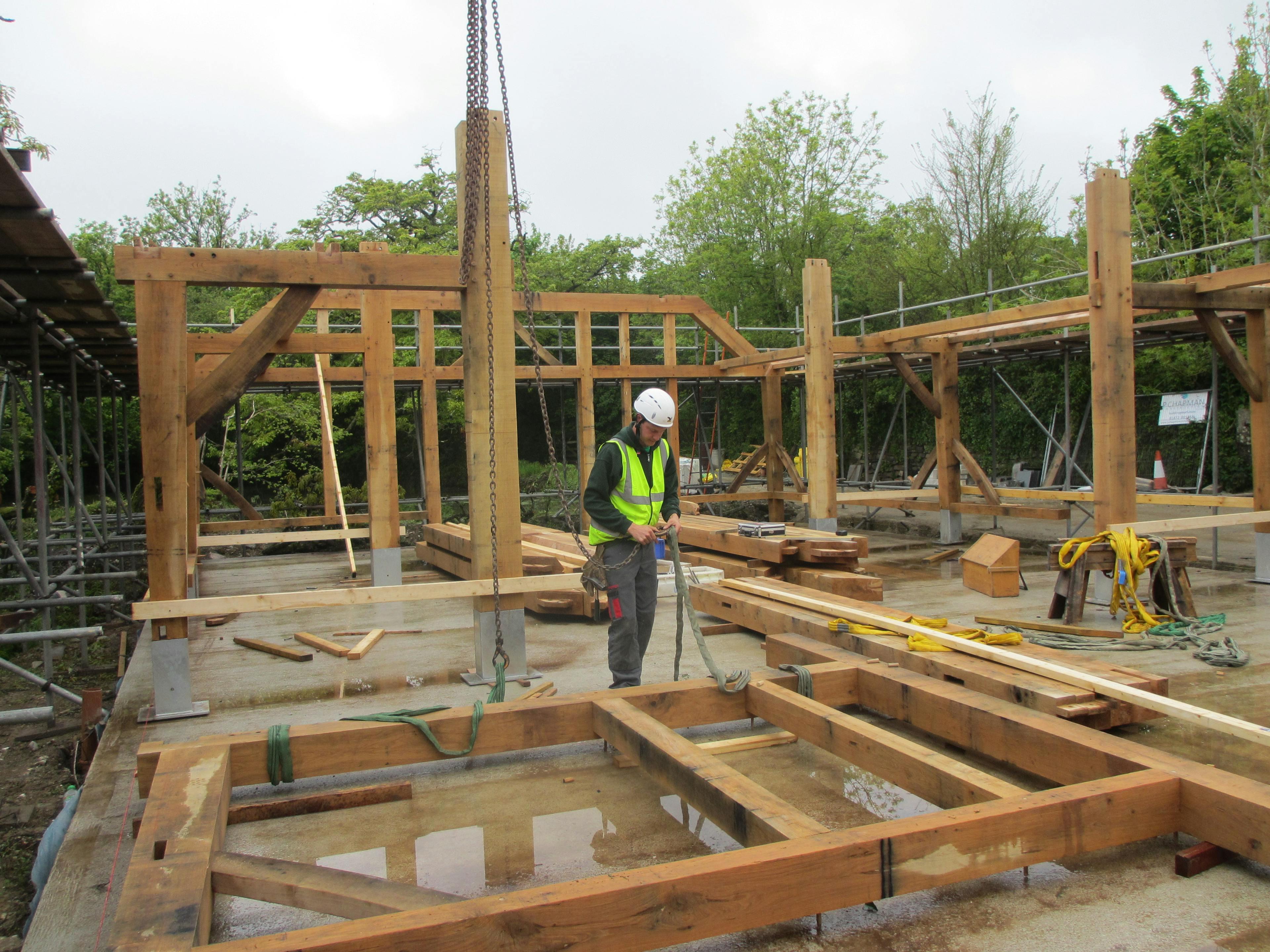 On a construction site a carpenter prepares a piece of the frame for an oak framed wedding barn to be installed
