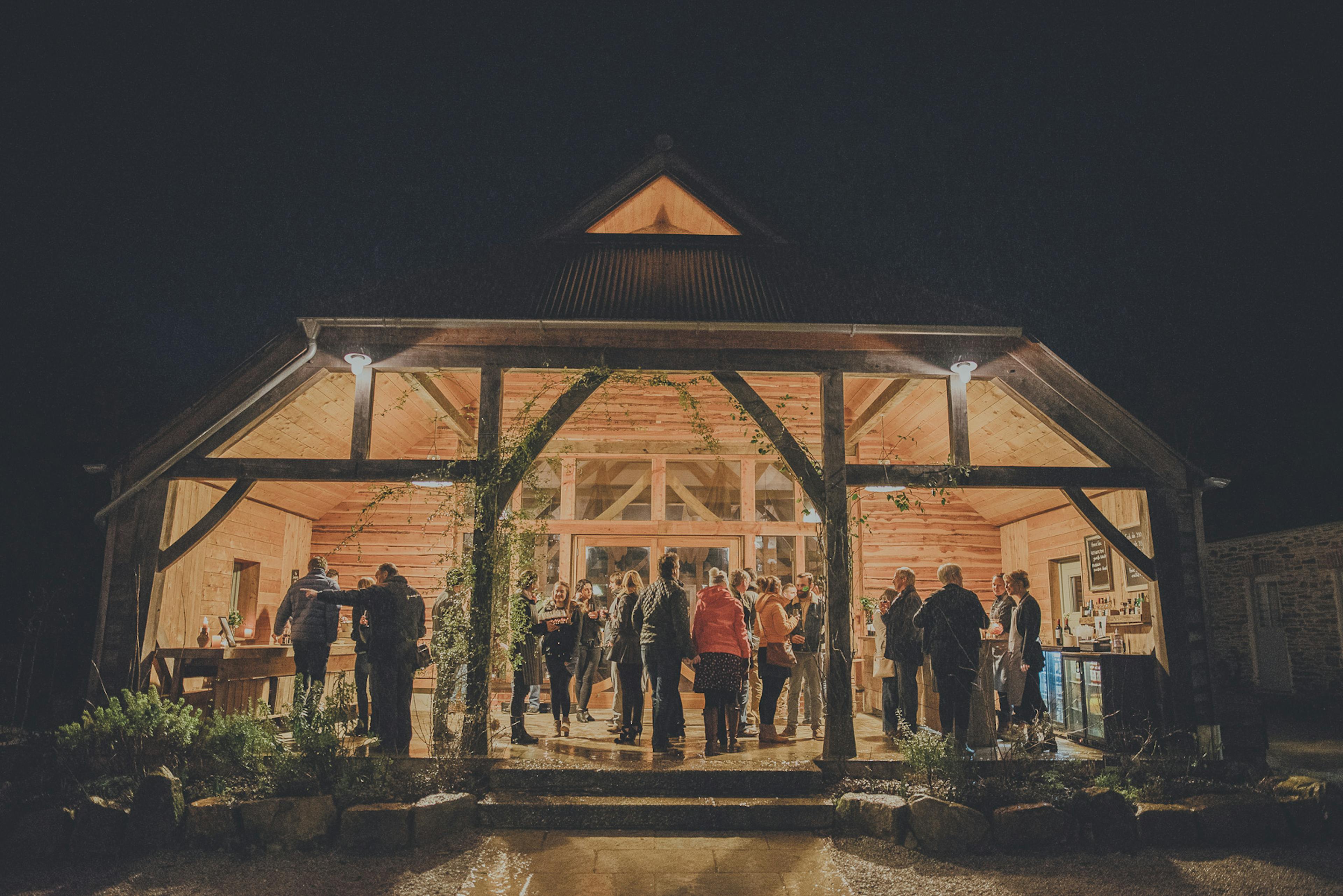 At night guests outside the entrance to an oak framed wedding barn