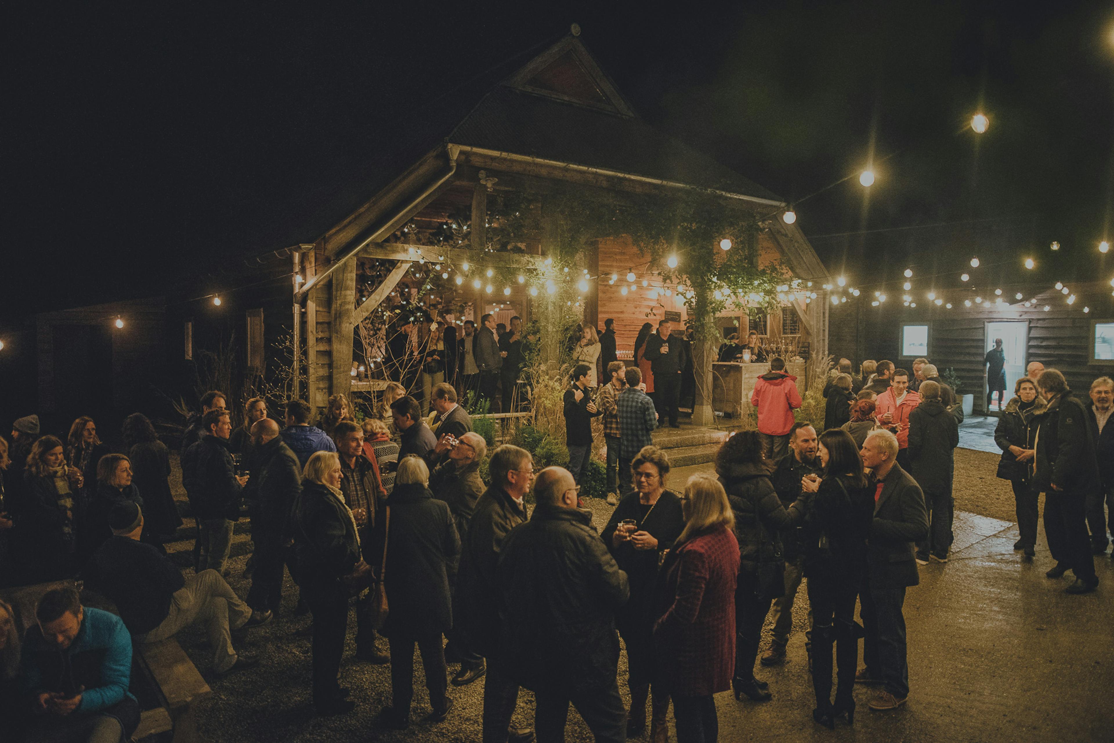 Guests at a wedding outside an oak framed wedding barn with pretty yellow lights