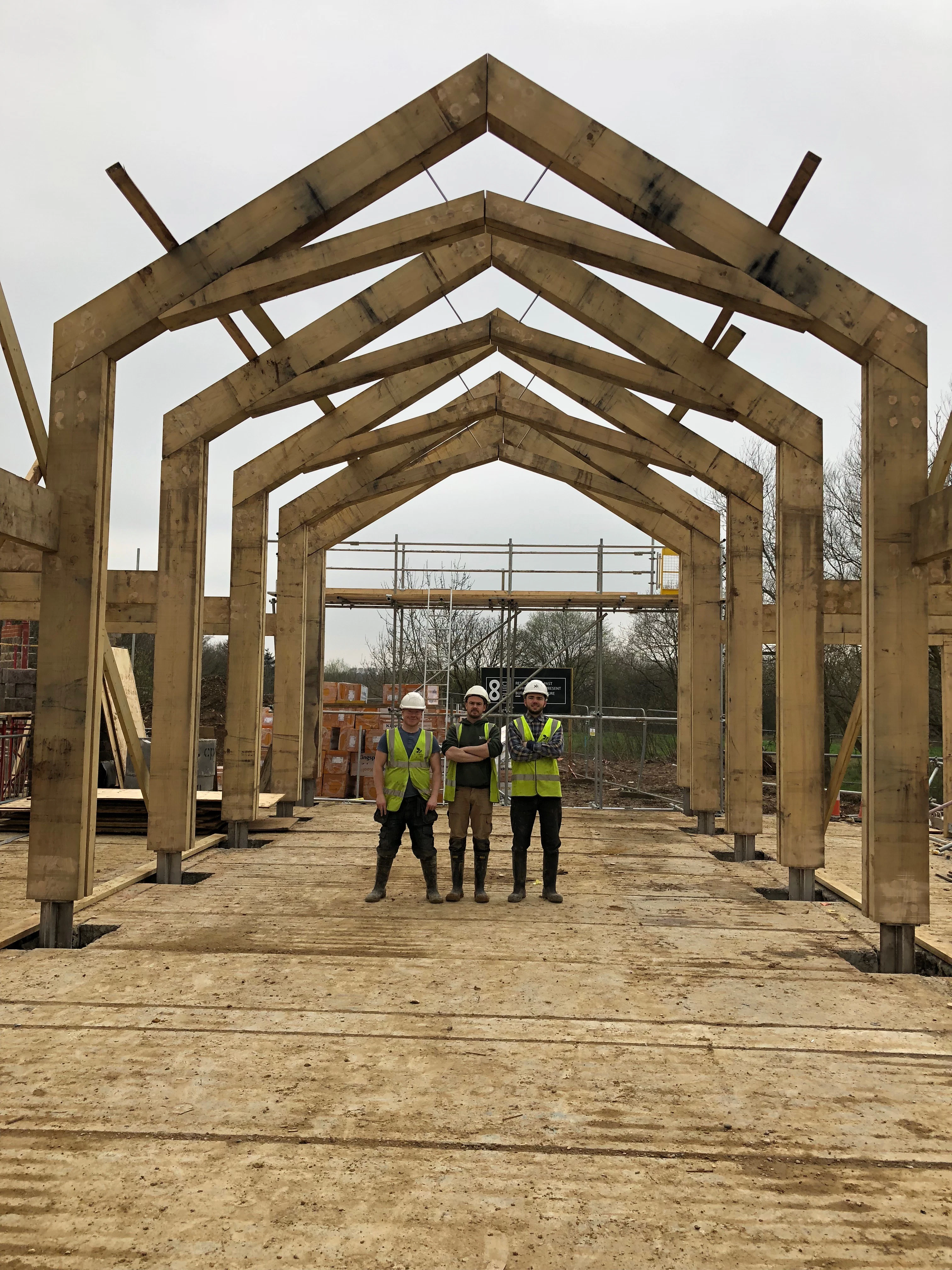On a construction site a team of carpenters stand under an oak portal frame during installation