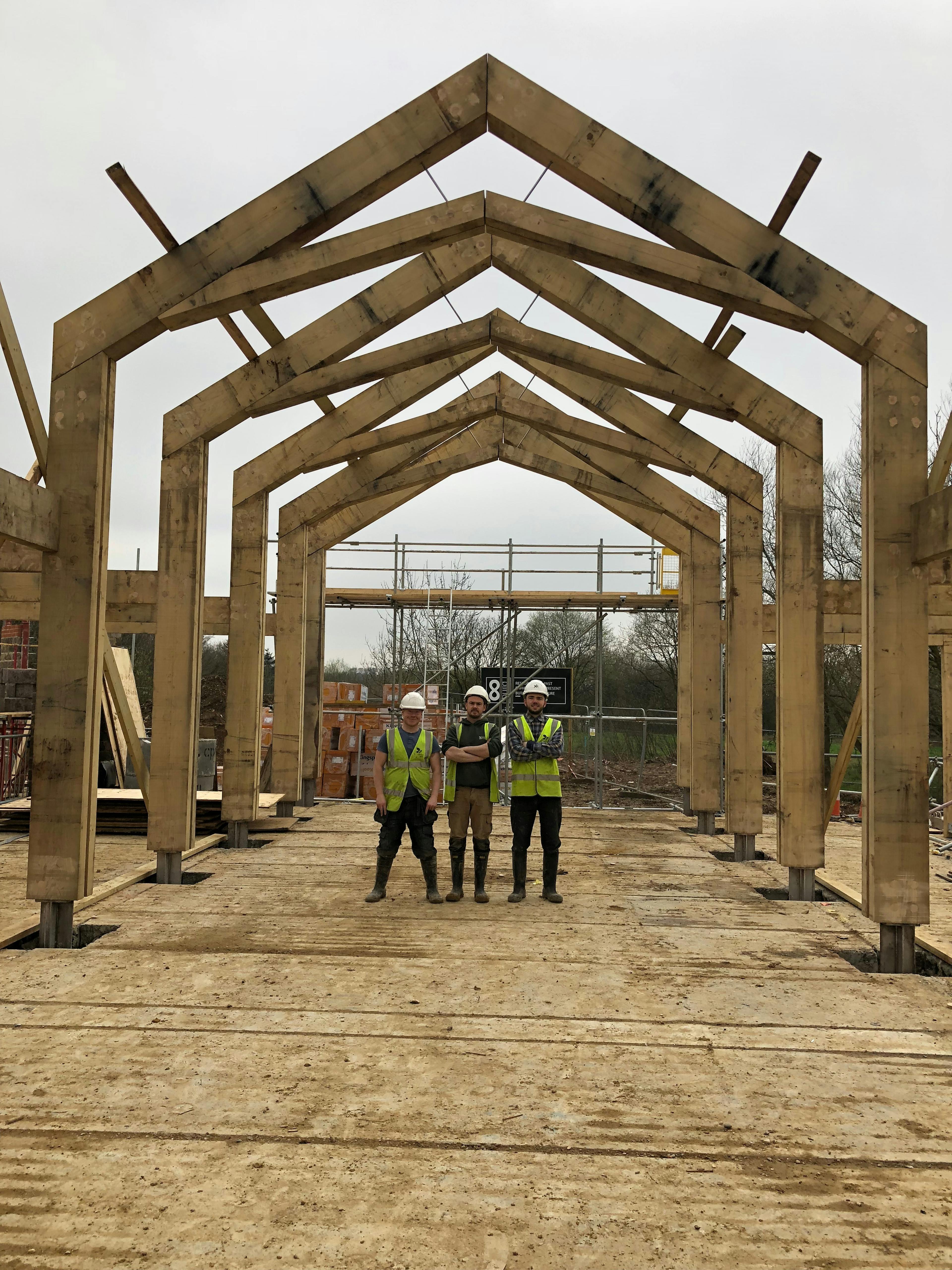 On a construction site a team of carpenters stand under an oak portal frame during installation